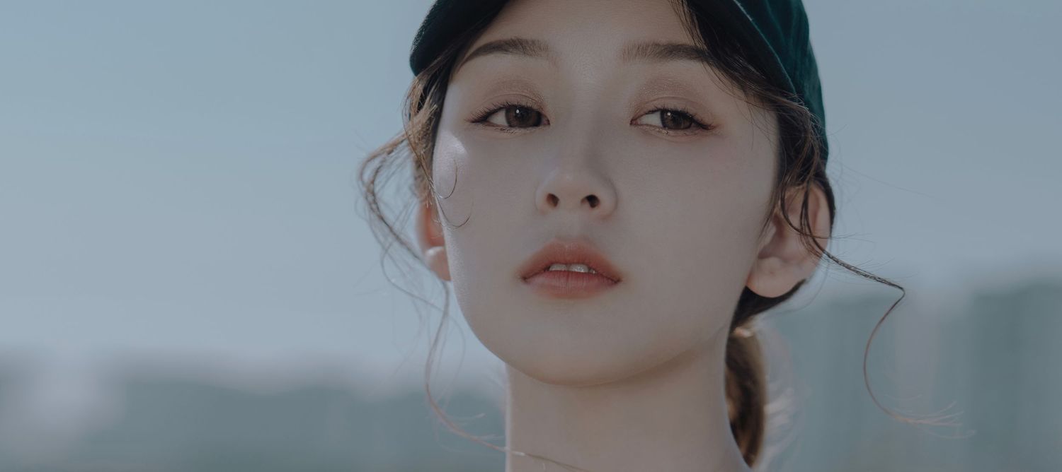 Close-up portrait of a young Asian woman with a black cap, soft skin, and a serene expression outdoors.