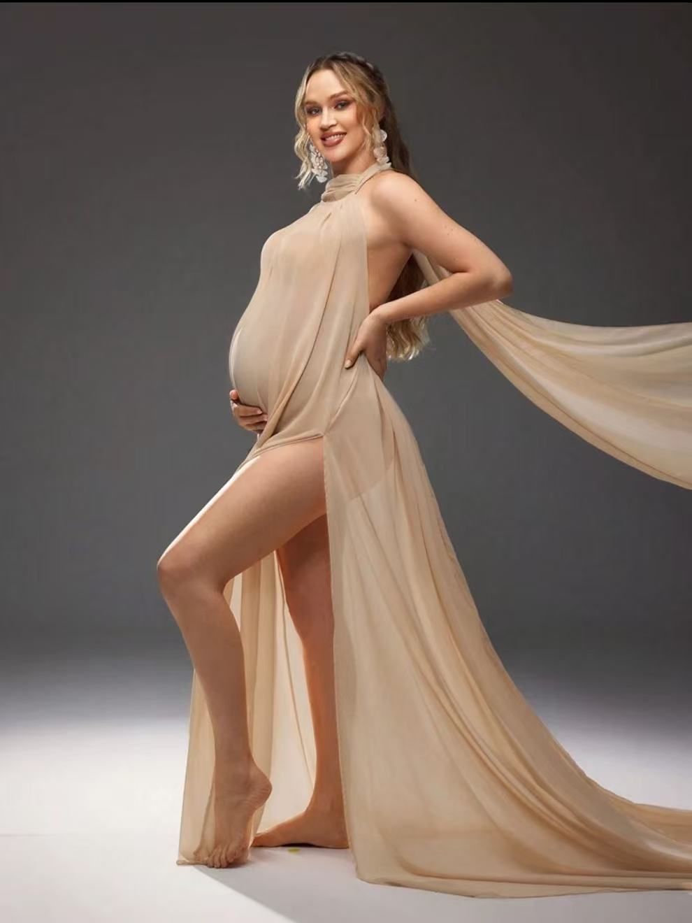 Pregnant woman in nude halter maternity gown with flowing cape and high slit.