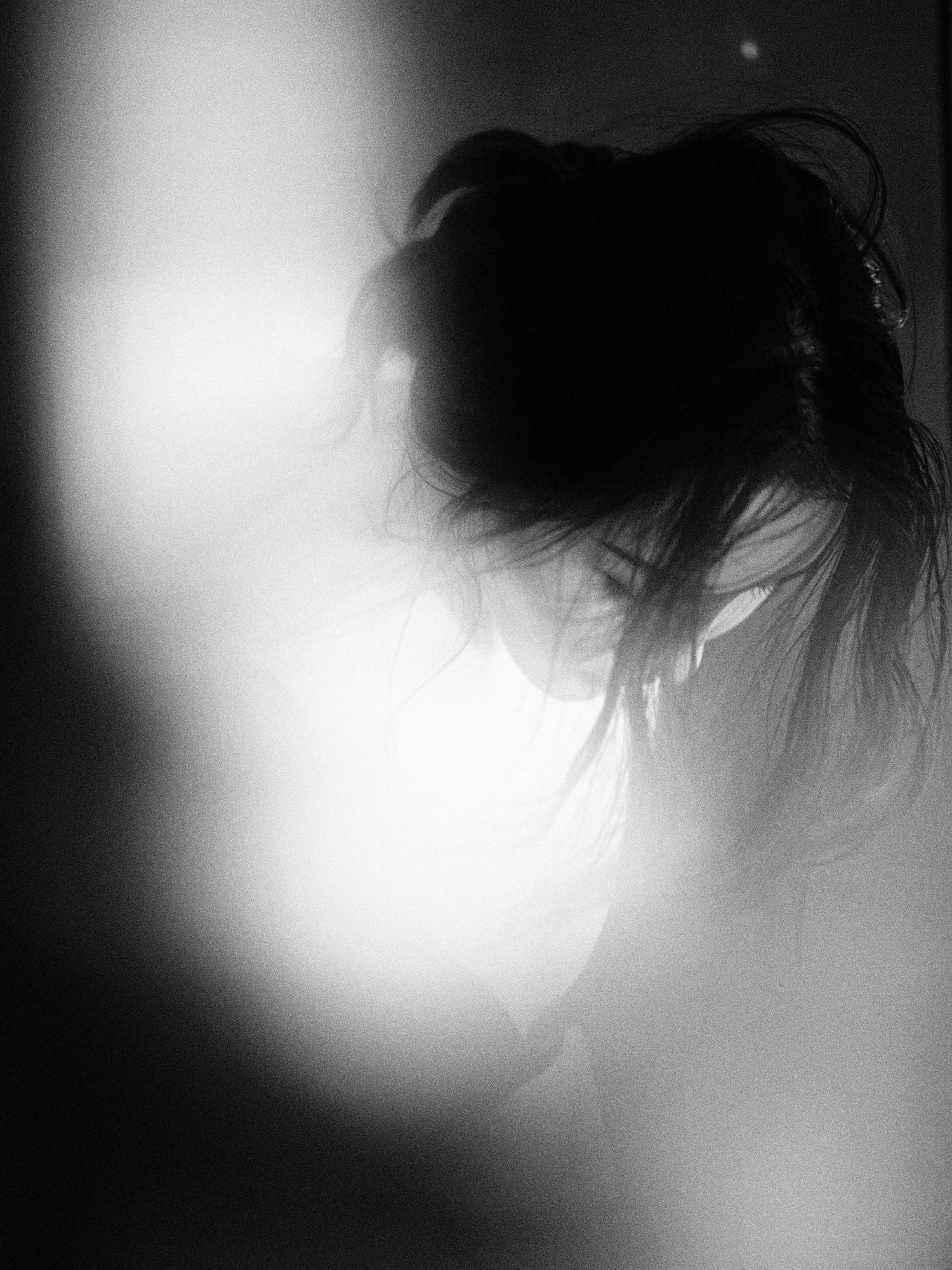 Artistic black and white silhouette of a woman with hair piled up, dramatically backlit creating a dreamlike effect.