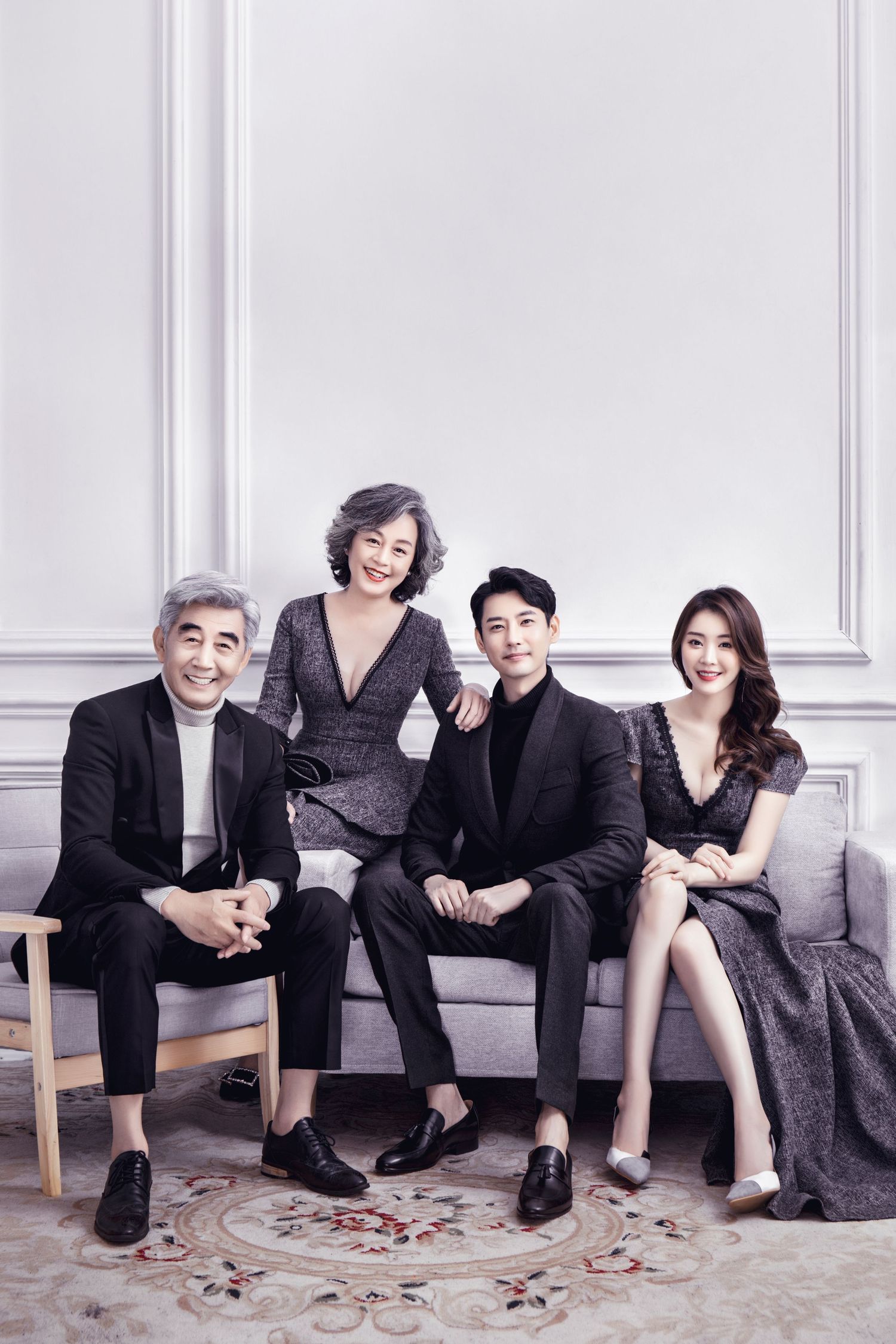 Stylish Asian family of four posing on a gray sofa in elegant formal wear for a professional portrait.