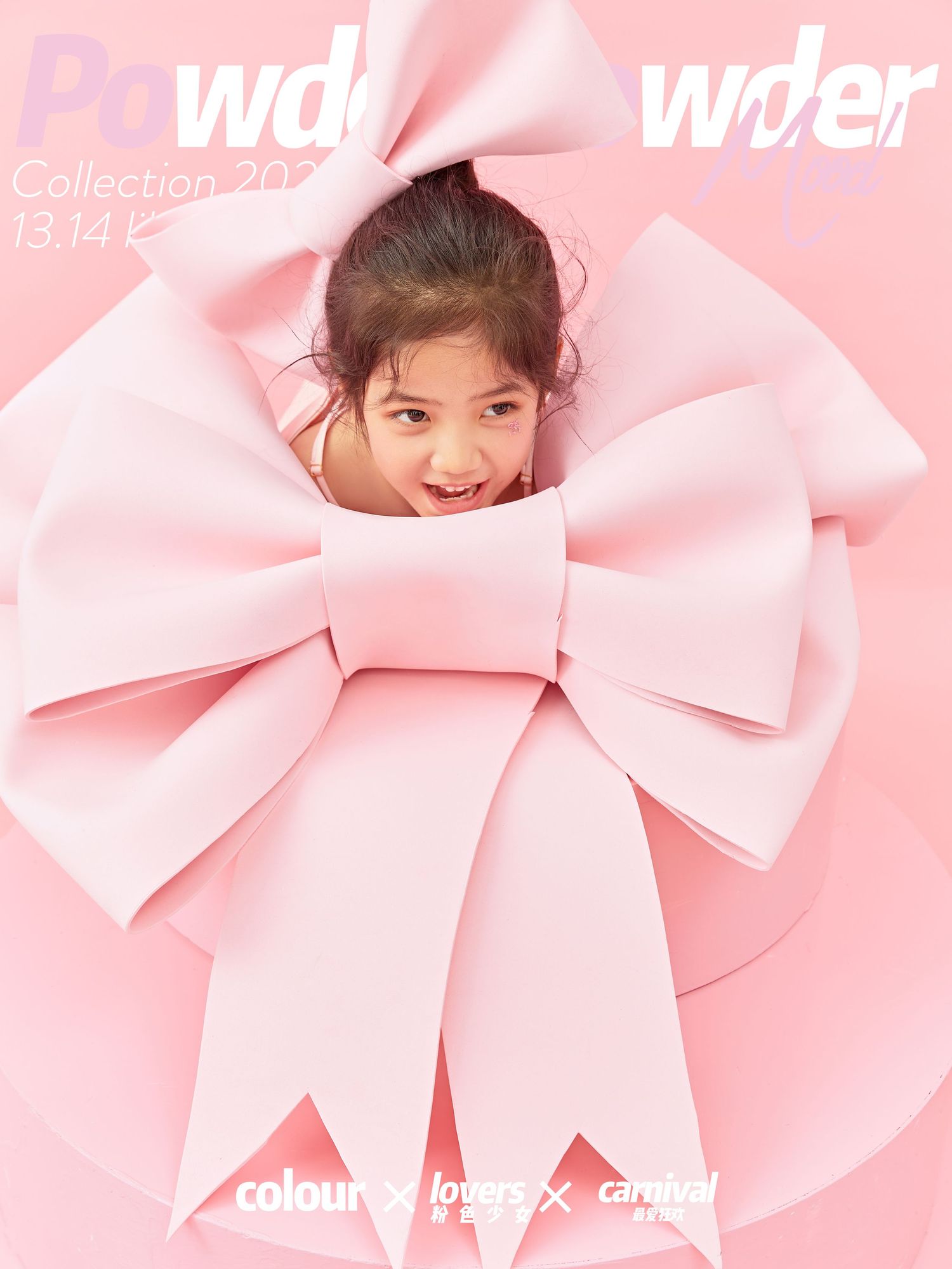 Smiling child peeking through large pink bow decoration in Powder Collection promotional photo.