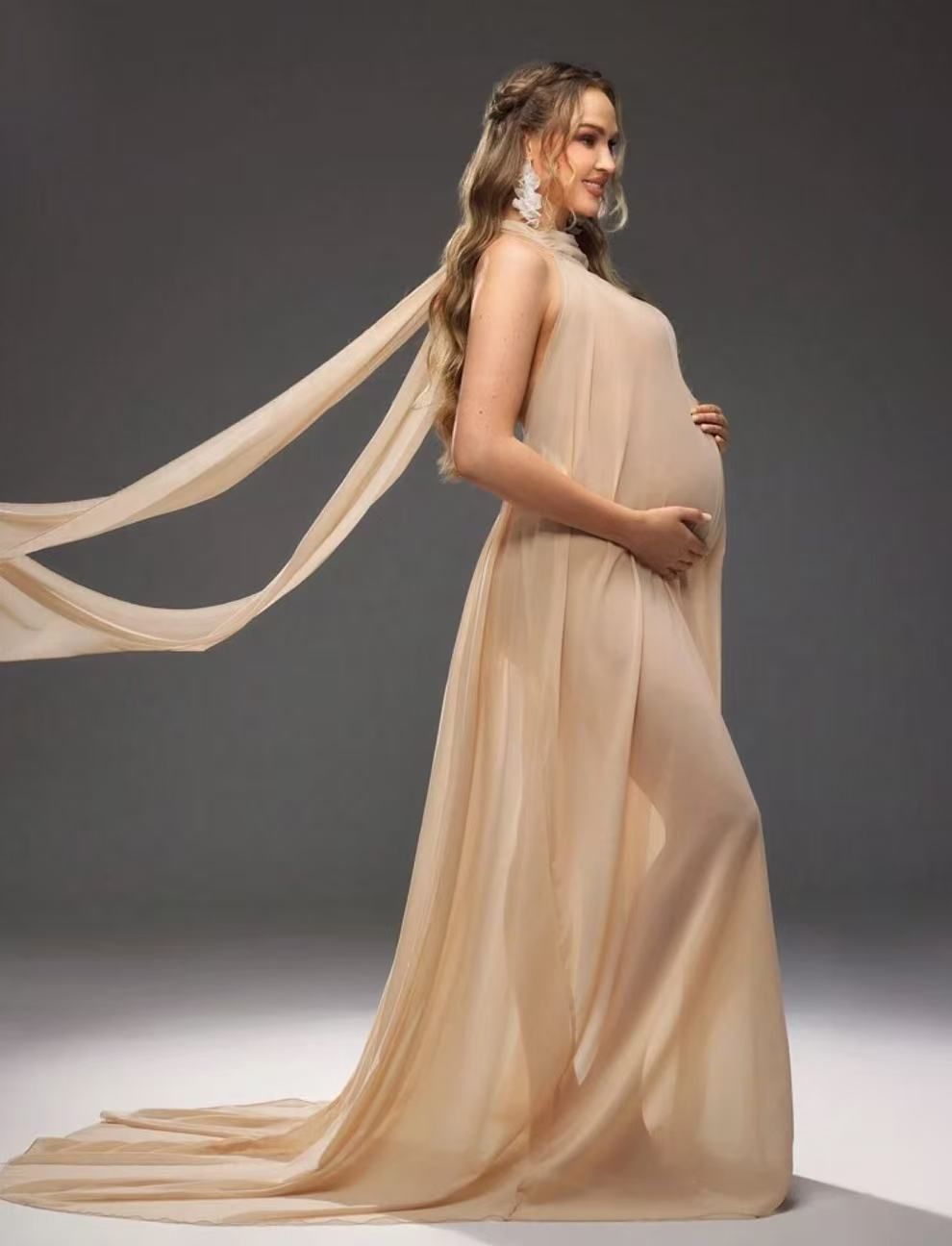 Pregnant woman in sheer champagne flowing maternity dress with long train.