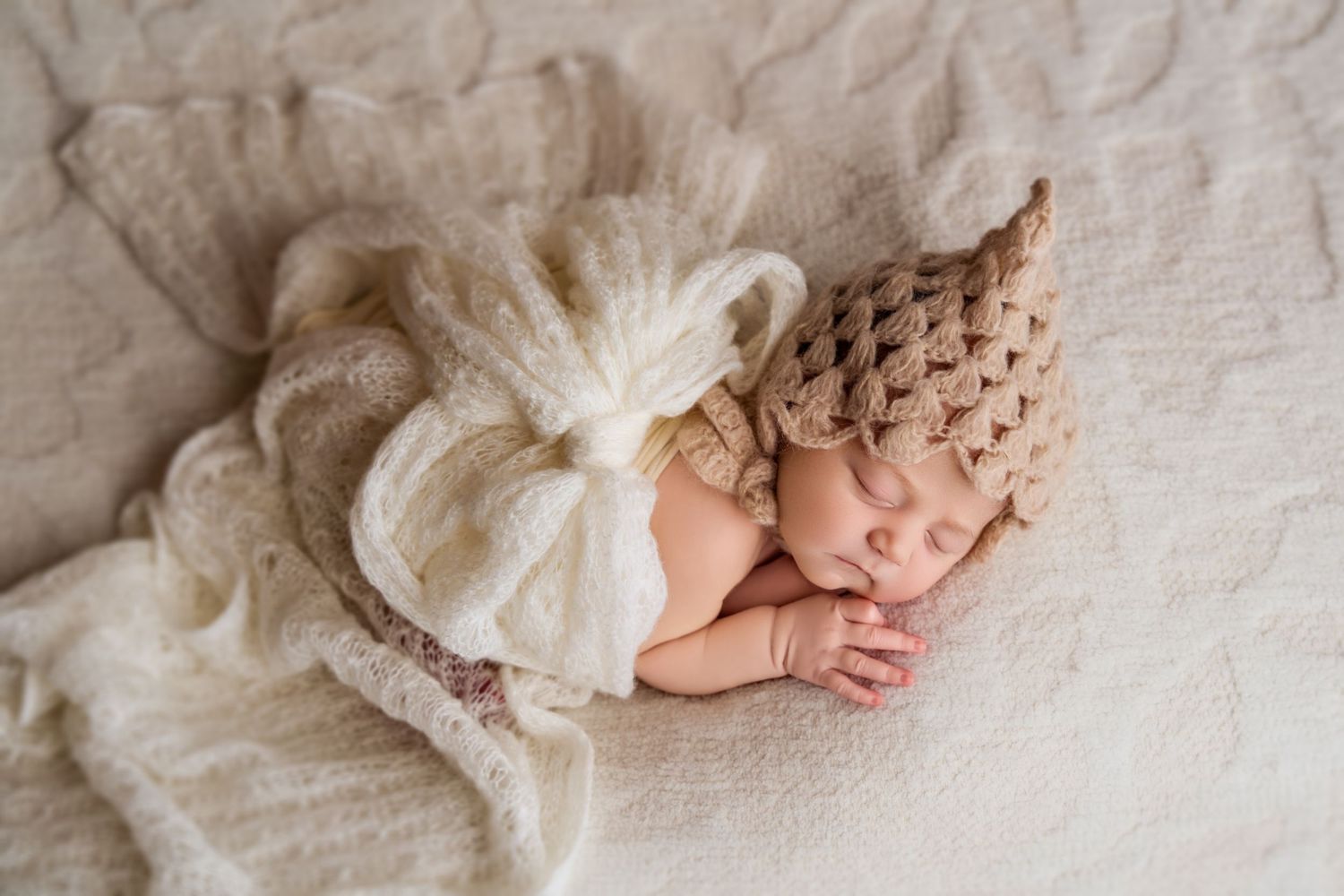 Sleeping newborn baby wearing a knit gnome hat on a cream blanket.