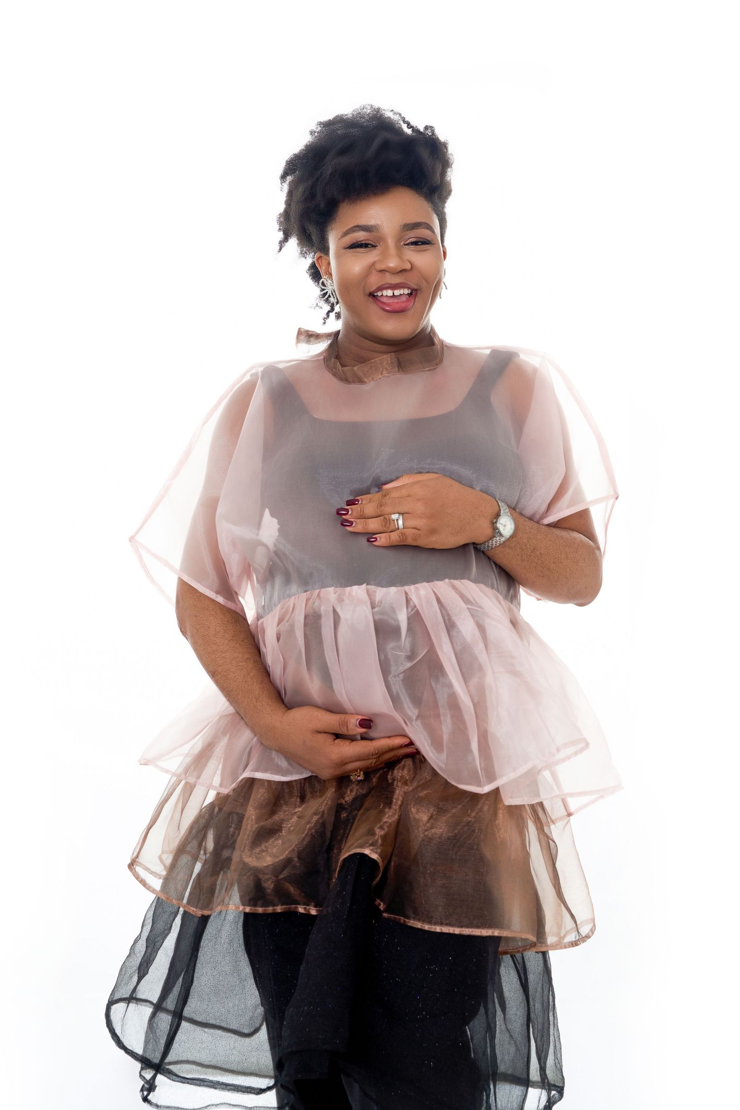 Smiling woman in sheer pink ruffled top poses confidently against white background, wearing a watch and ring.