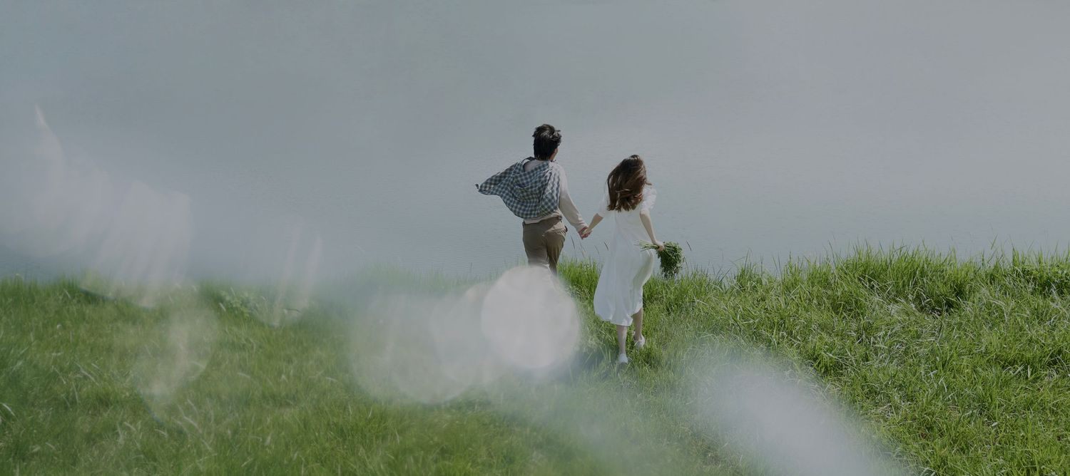 Couple holding hands walking on green hillside together.