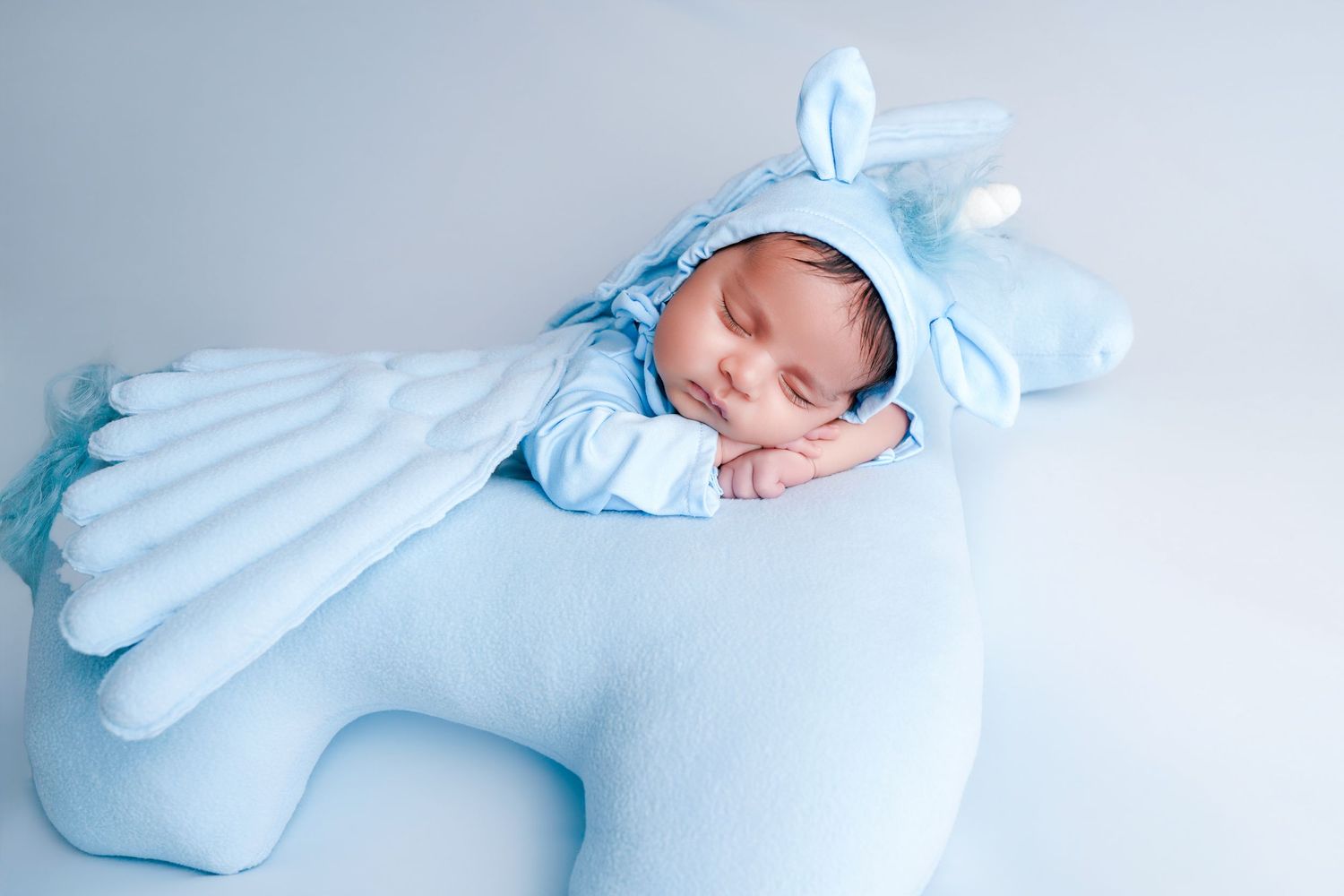 Newborn baby sleeping peacefully on a blue unicorn pillow wearing a matching blue unicorn costume.