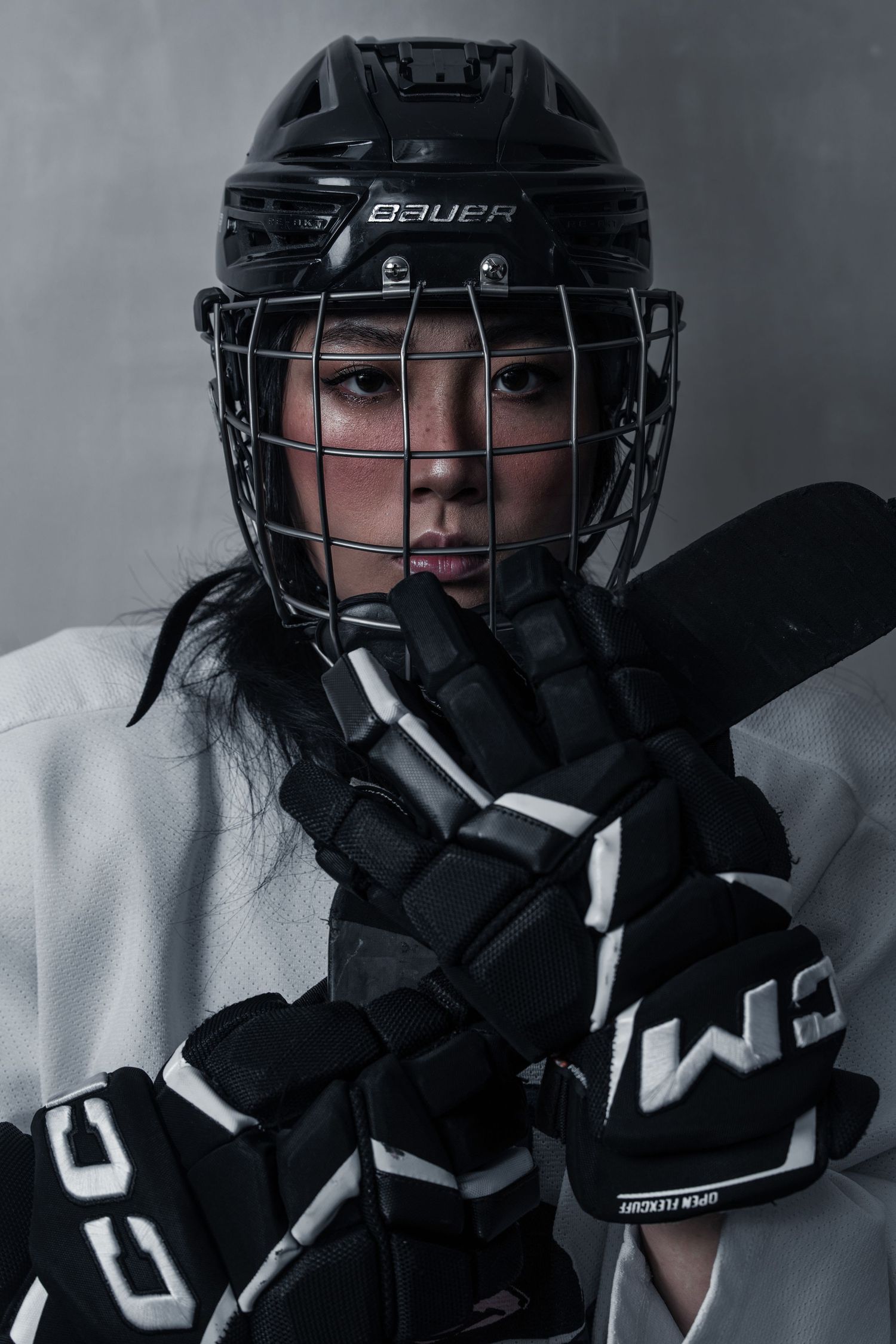 Female ice hockey player in Bauer helmet with cage visor holding stick, wearing black and white protective gear.