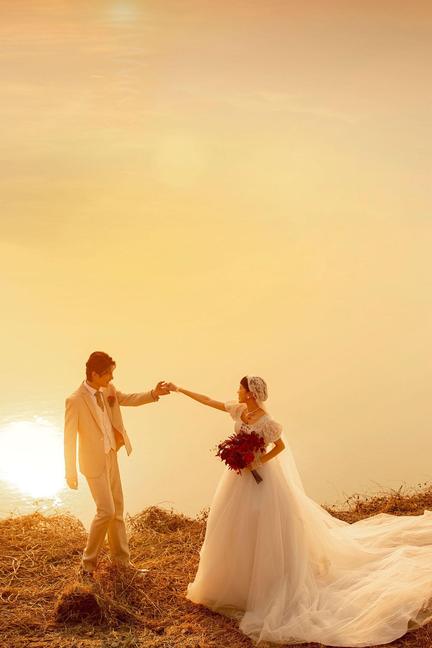 Bride and groom hold hands at golden sunset overlooking a shimmering lake in outdoor wedding photo.