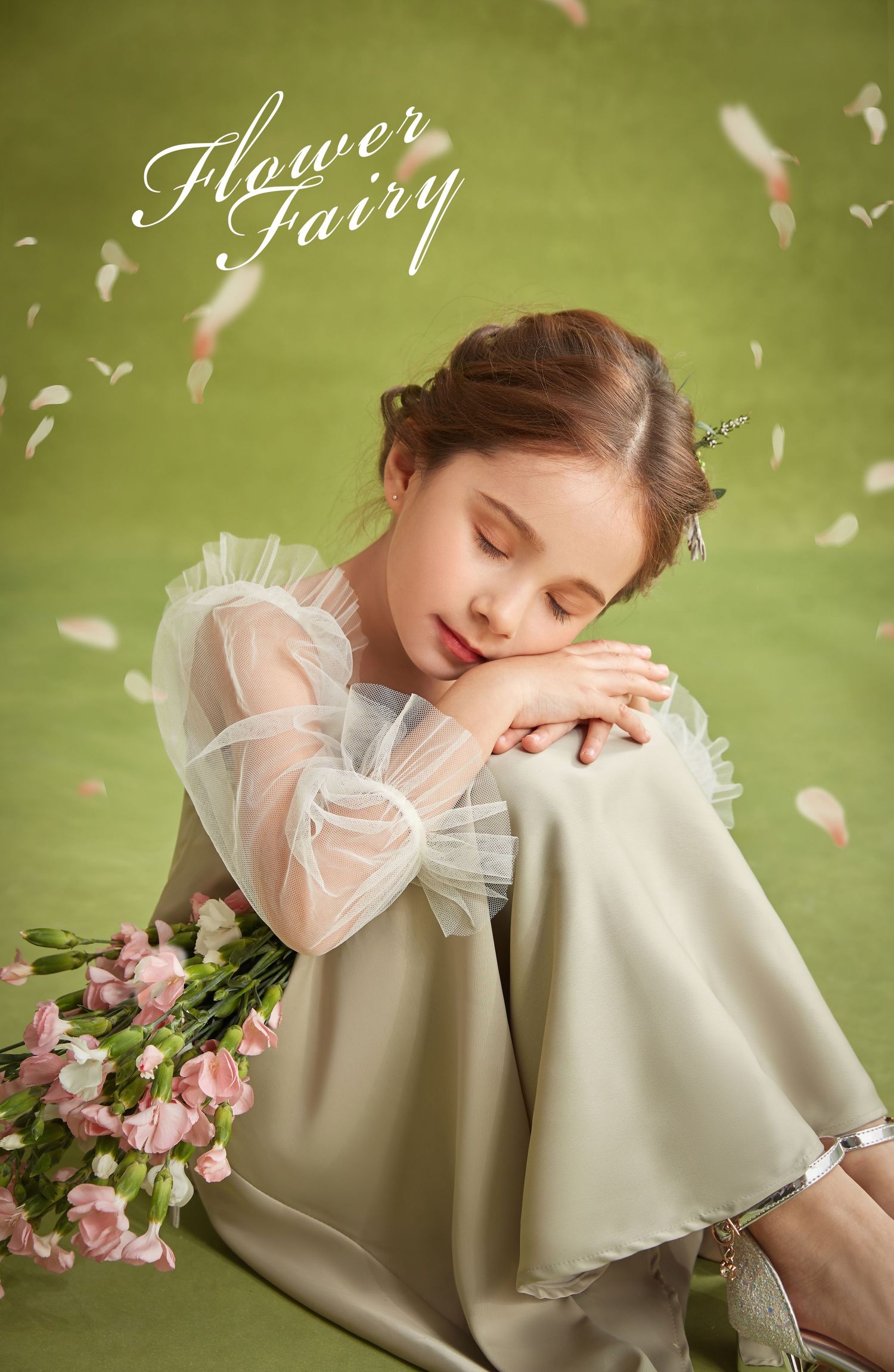Young girl in sage green dress with sheer sleeves rests with pink flowers, petals falling.