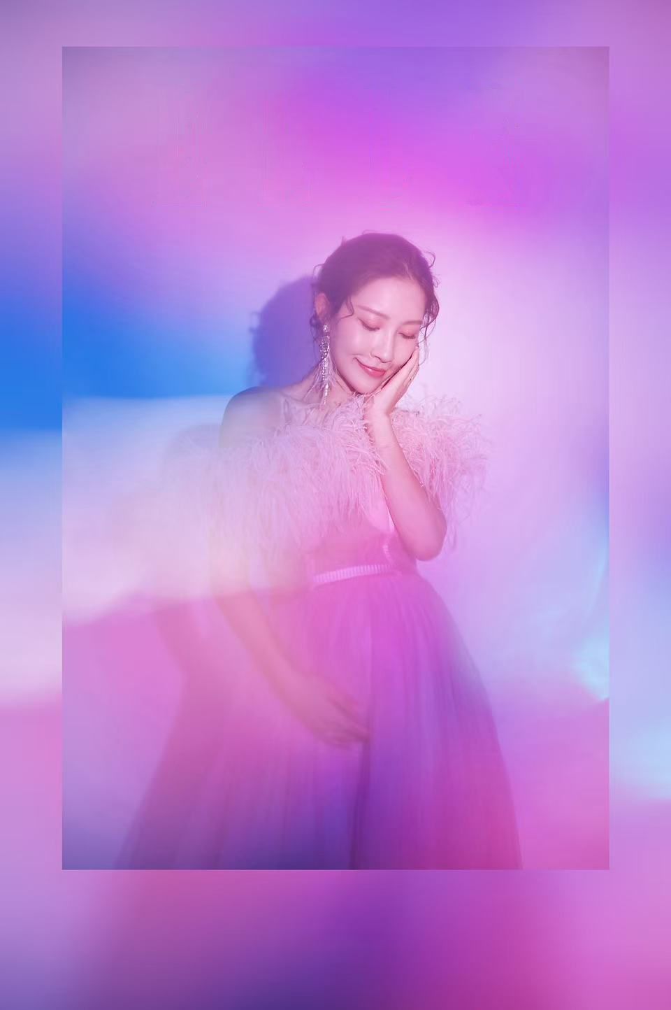 A woman in a pink feathered tulle gown poses dreamily against a vibrant purple and blue gradient background.