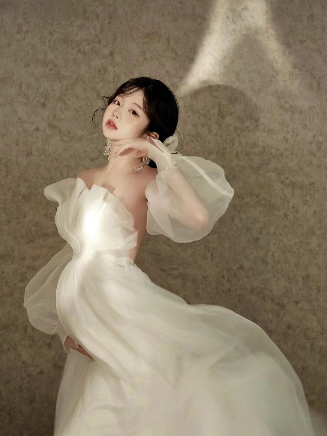 Woman in elegant white off-shoulder tulle bridal gown posing gracefully against a textured neutral background.