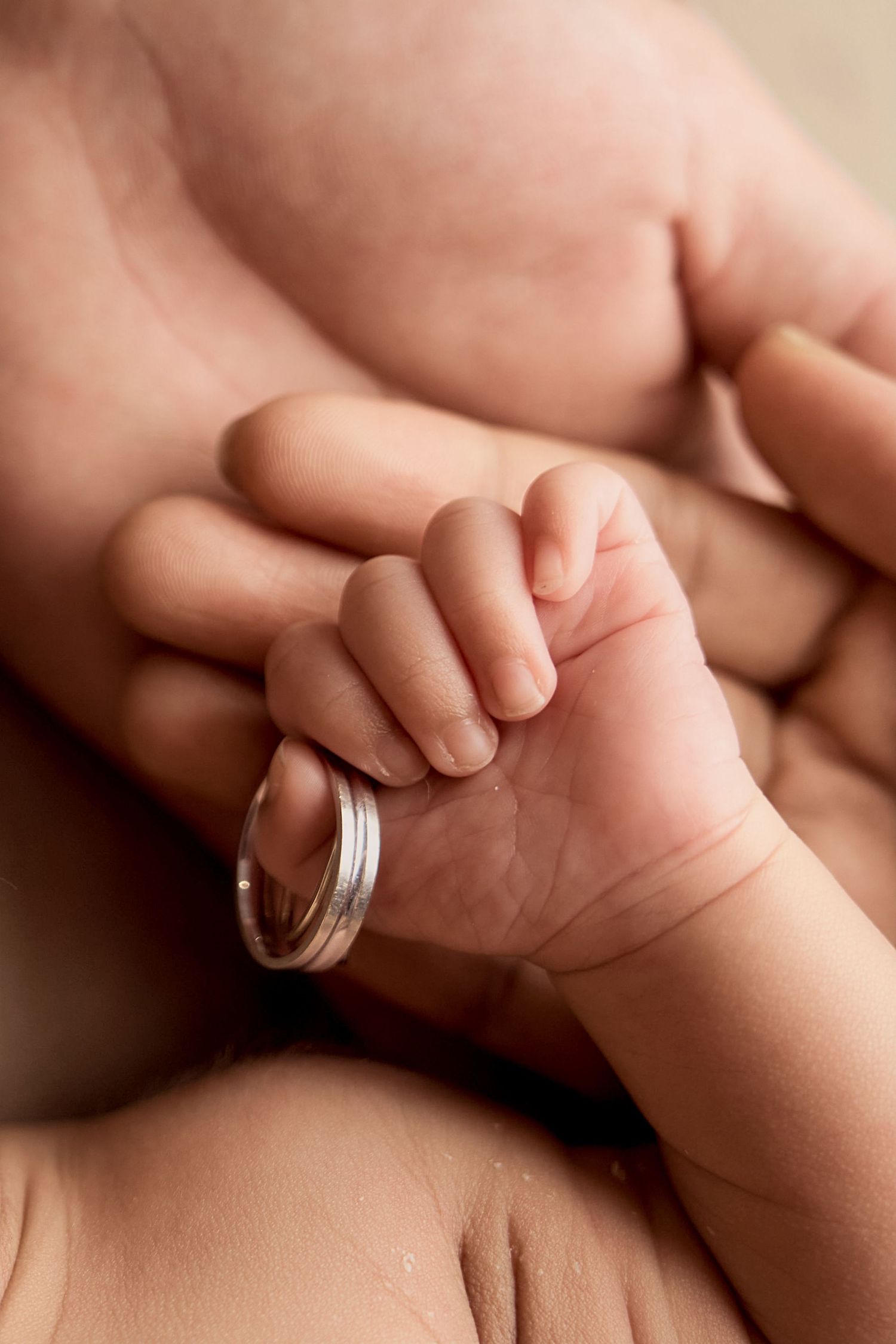 A newborn baby's tiny hand gently gripping an adult's finger wearing a silver wedding ring.
