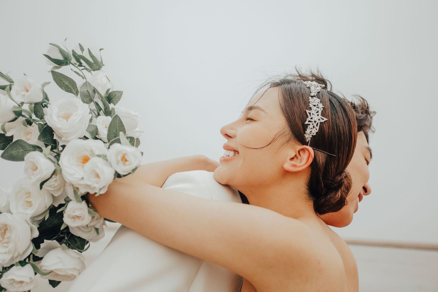 Smiling bride hugging groom while holding white flower bouquet.