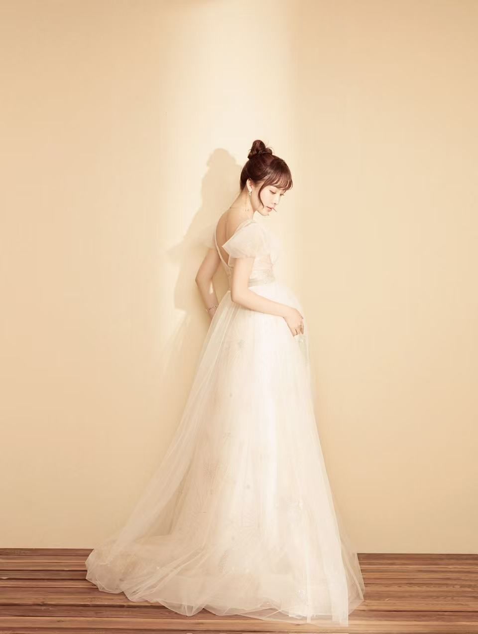 Elegant woman in off-shoulder white tulle ball gown wedding dress poses gracefully against warm beige wall.