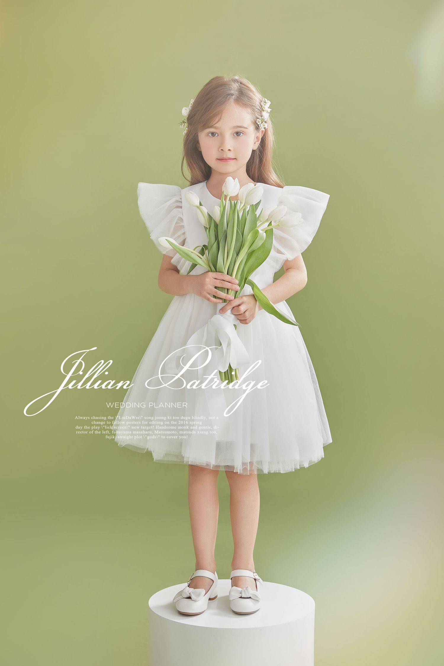 Young girl in white tulle dress stands on pedestal holding white tulips on green background.