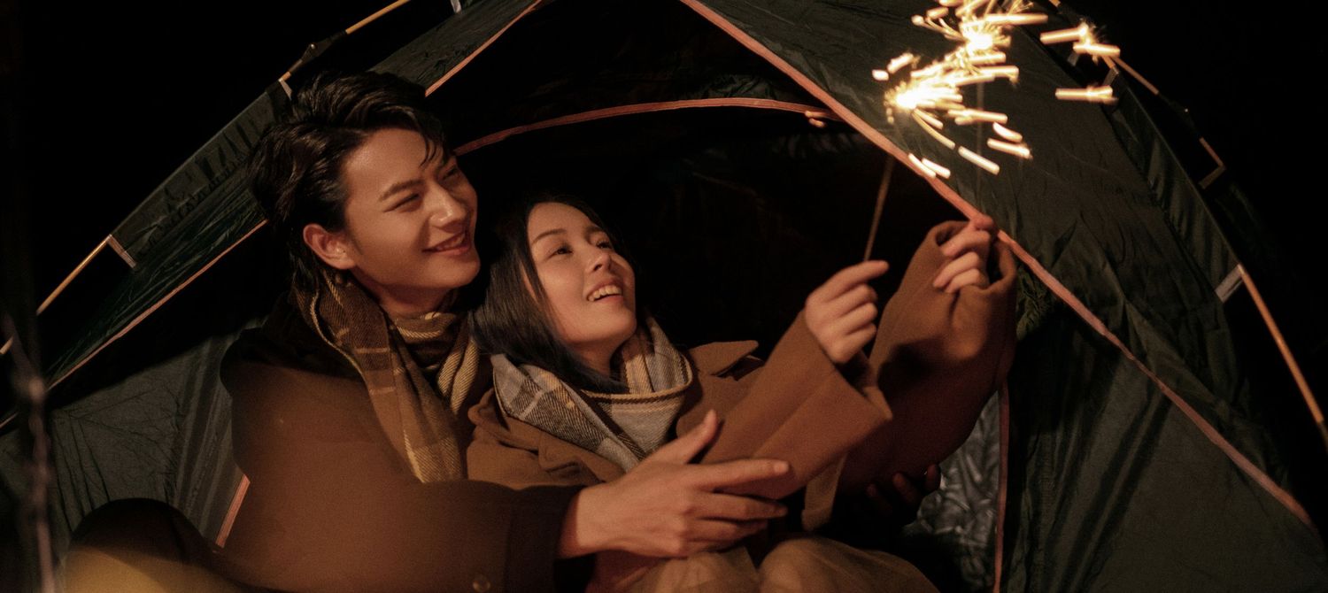 Couple sharing a romantic moment inside a tent with sparklers glowing in the dark night.