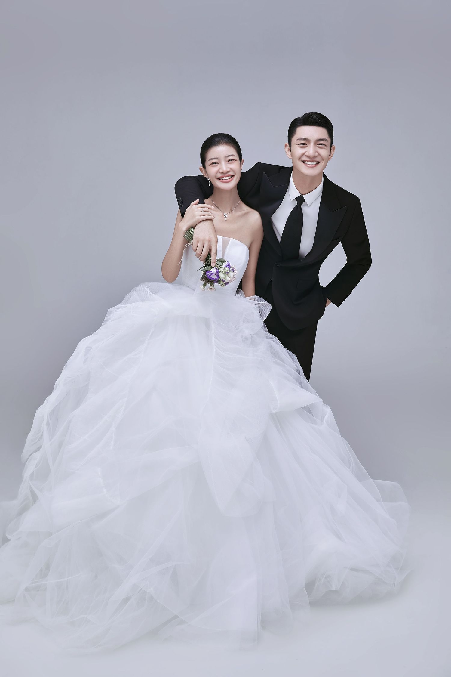 An elegant bride in a white ball gown poses with a groom in a black tuxedo for wedding photos.