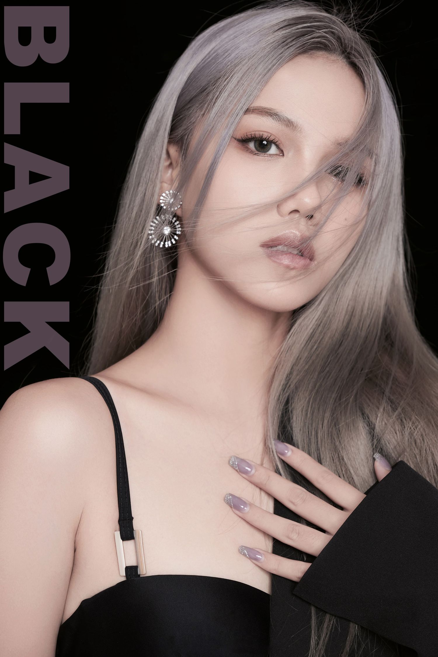 Young woman with silver-gray hair wearing a black dress and floral earrings poses against a dark background.