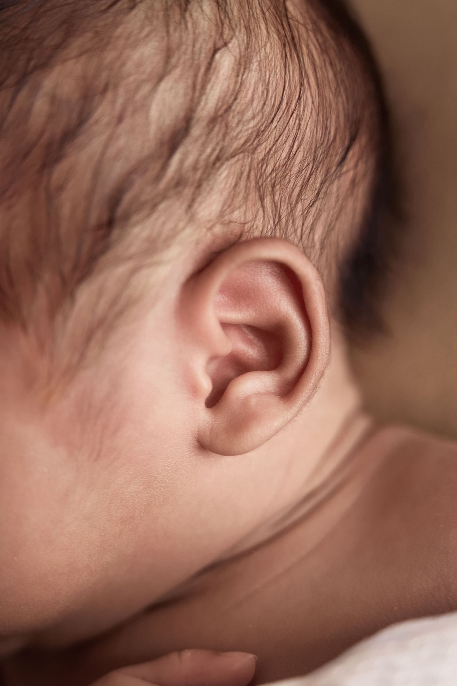 Close-up of a newborn baby's ear with fine dark hair, showcasing delicate skin texture.