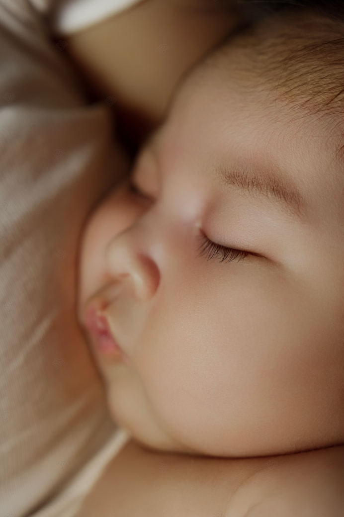 Close-up of a peacefully sleeping newborn baby with soft skin and delicate features resting on a warm blanket.