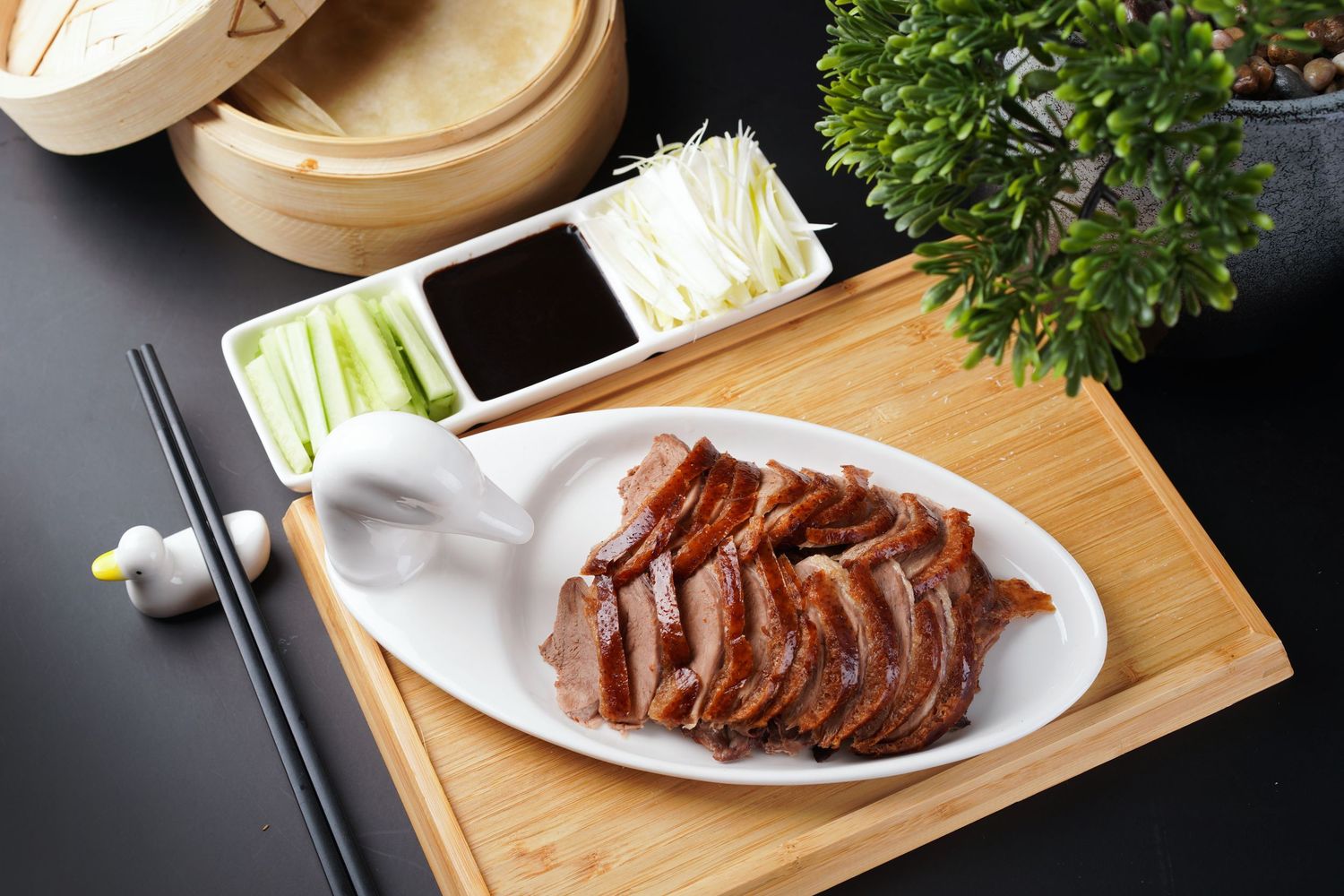 Traditional Peking duck dish served with hoisin sauce, scallions and steamed wrappers on wooden board.
