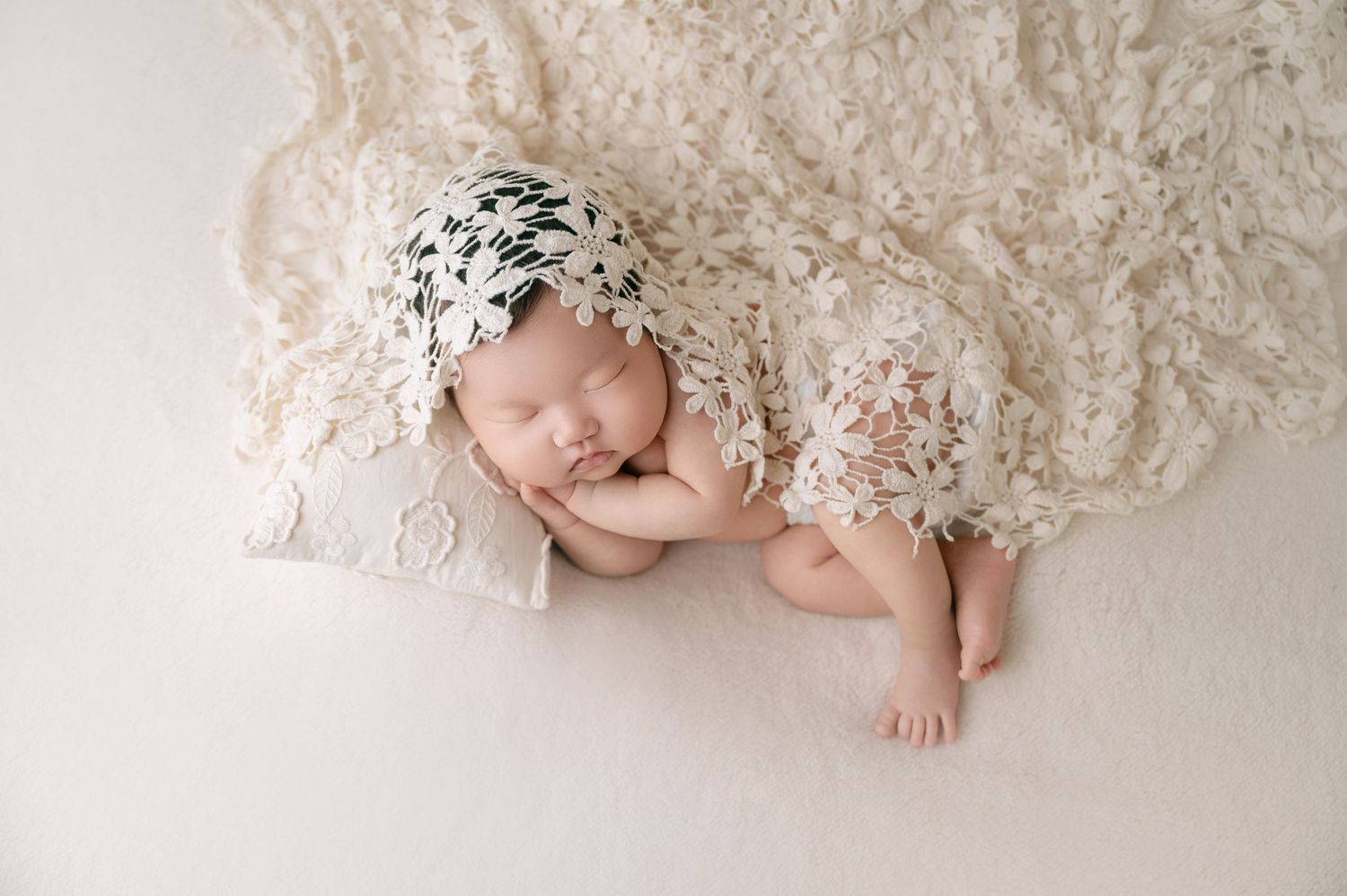 Sleeping newborn baby in black and white star bonnet on cream lace blanket.