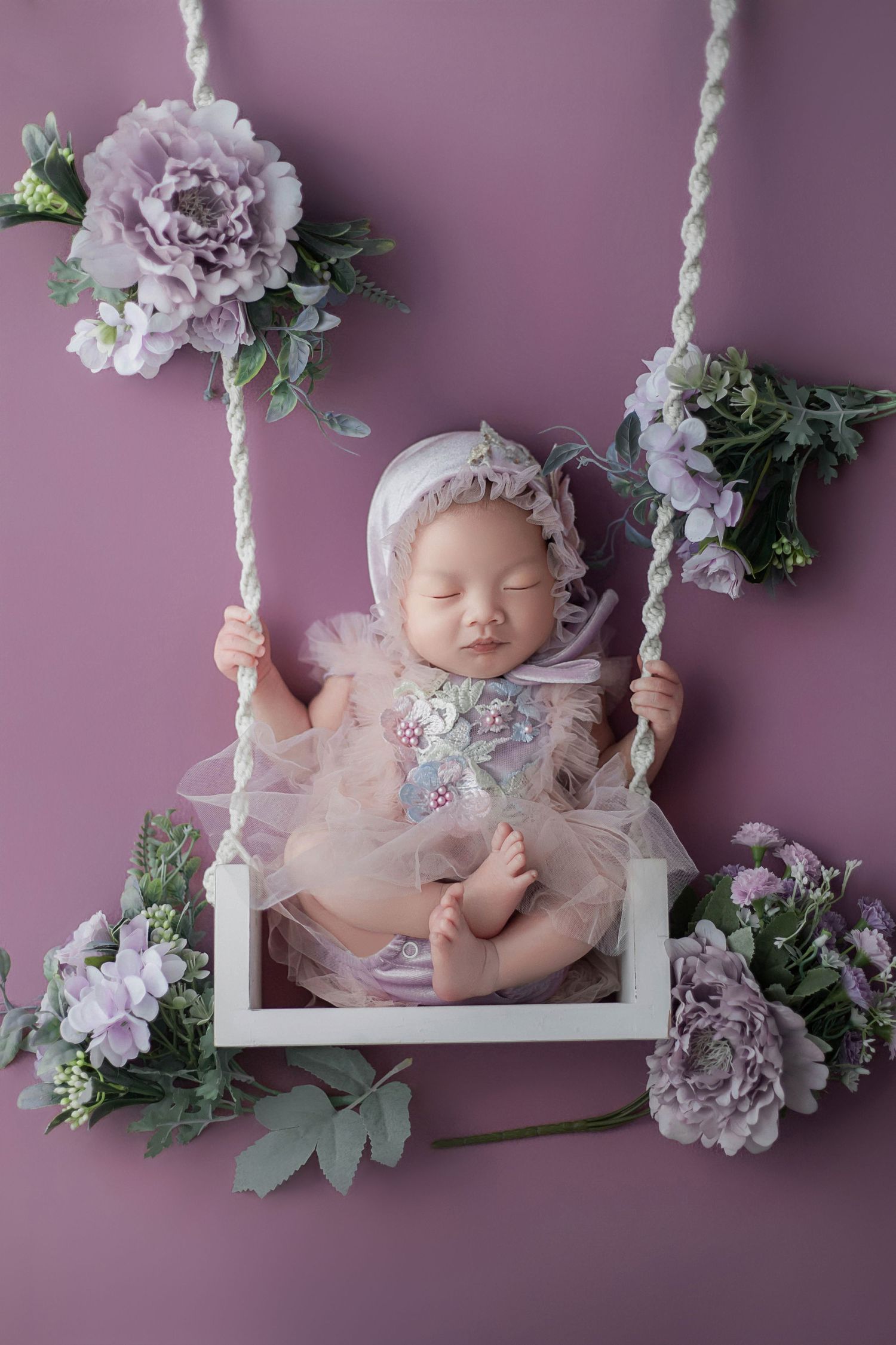 Peaceful newborn baby sleeping in a white swing decorated with purple flowers and tulle dress.
