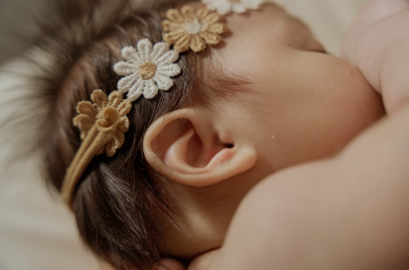 Close-up of a sleeping newborn baby wearing a delicate gold and white floral crochet headband.