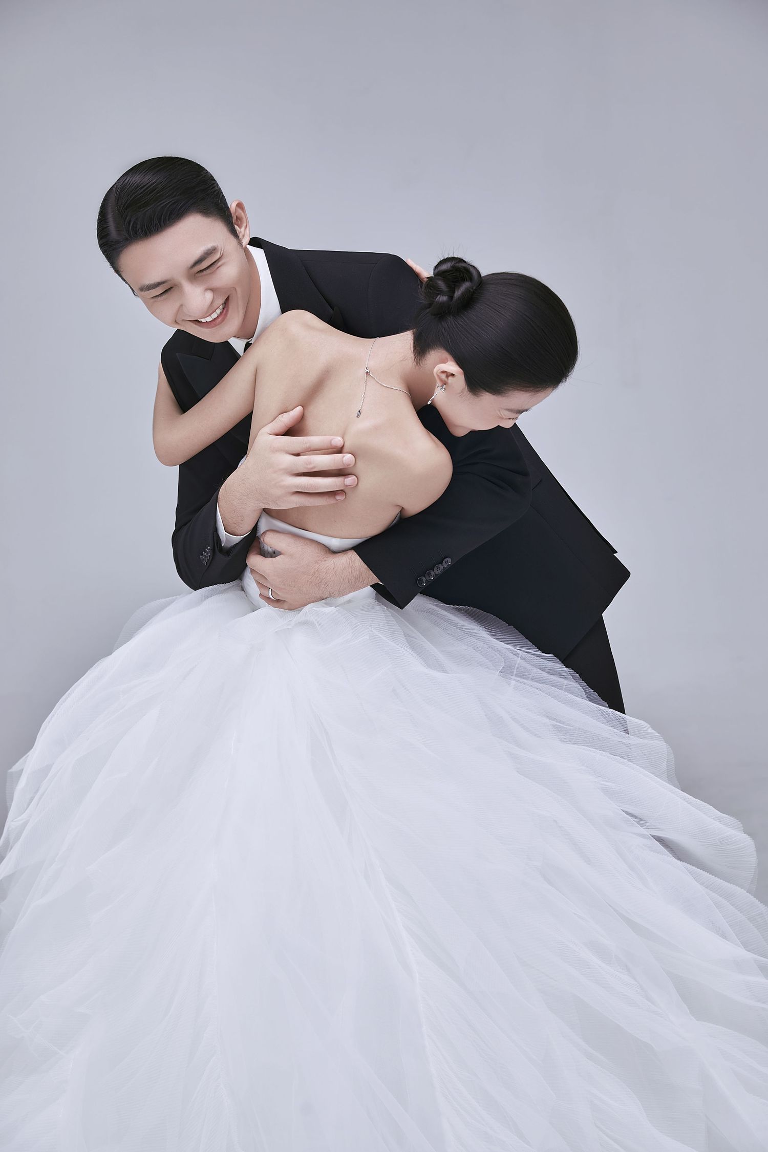 Groom in black tuxedo embracing bride in white ballgown wedding dress in romantic studio portrait.