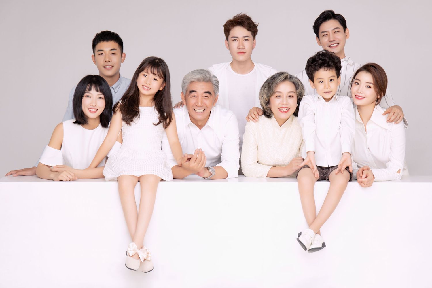 A cheerful multigenerational Asian family in white outfits posing together in a bright studio portrait.