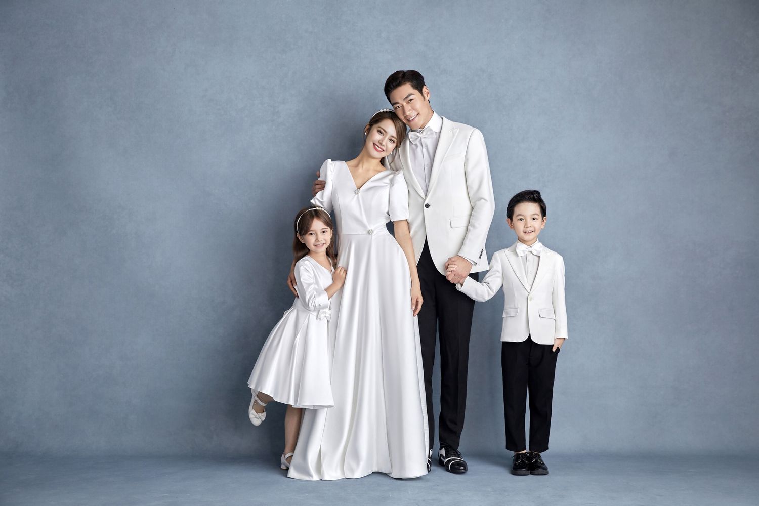 Family of four in white formal outfits posing together for an elegant studio portrait photo.