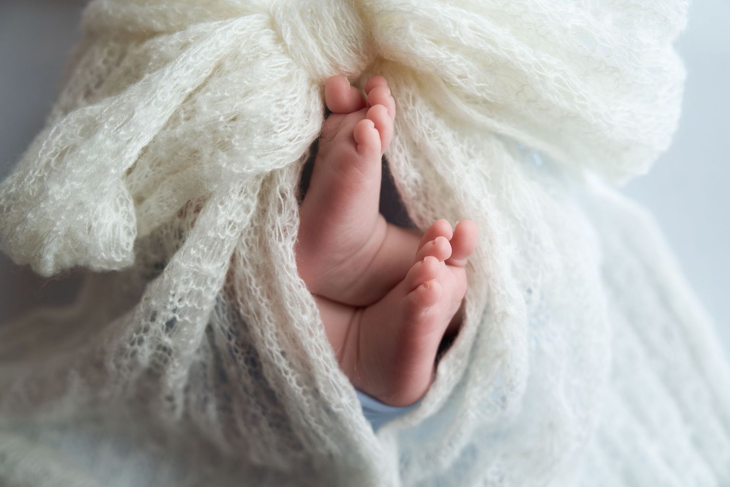Newborn baby feet peeking out of a soft white lace wrap, close-up photography.