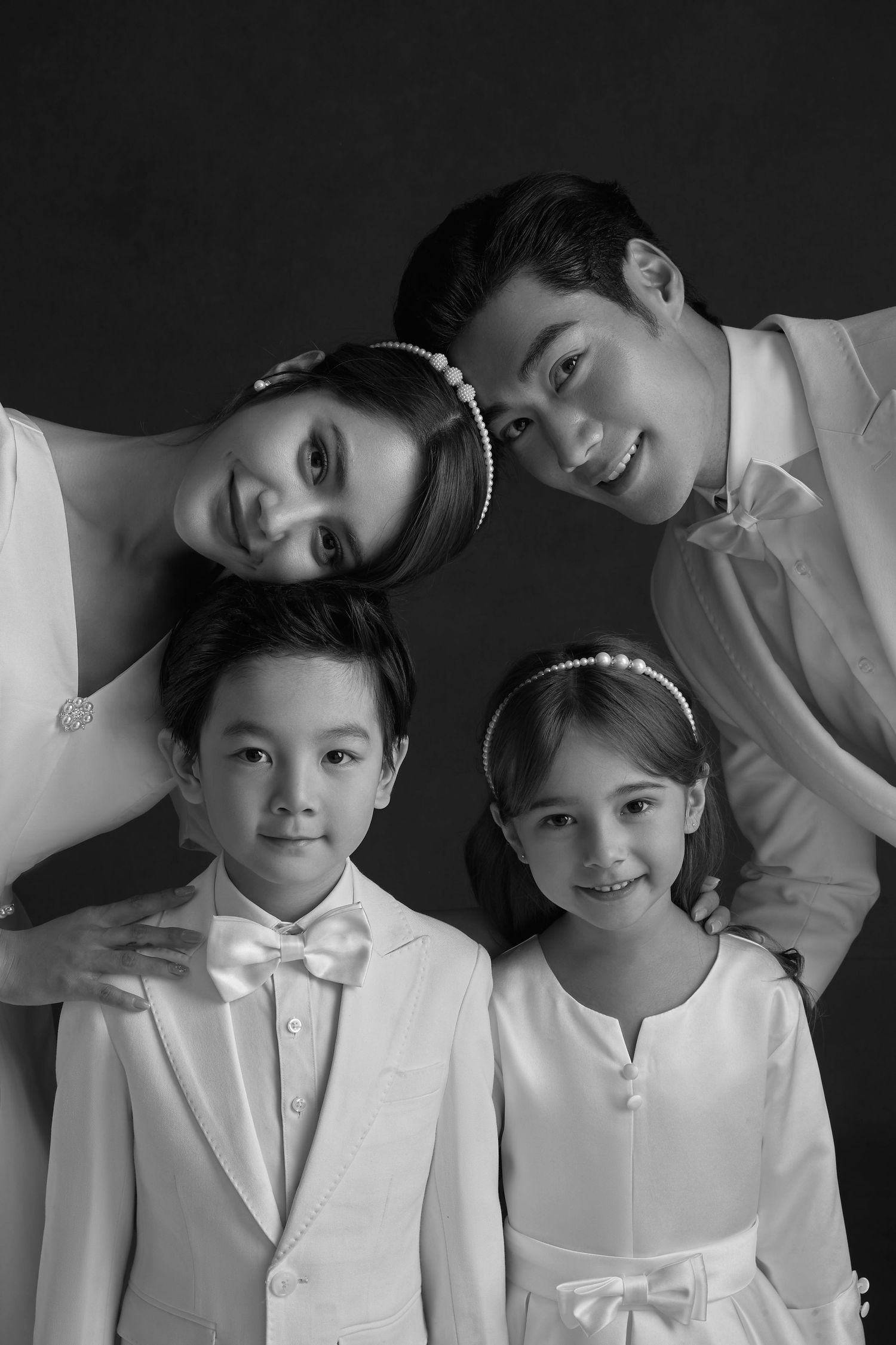 Black and white family portrait of parents and two children in formal white attire smiling together.