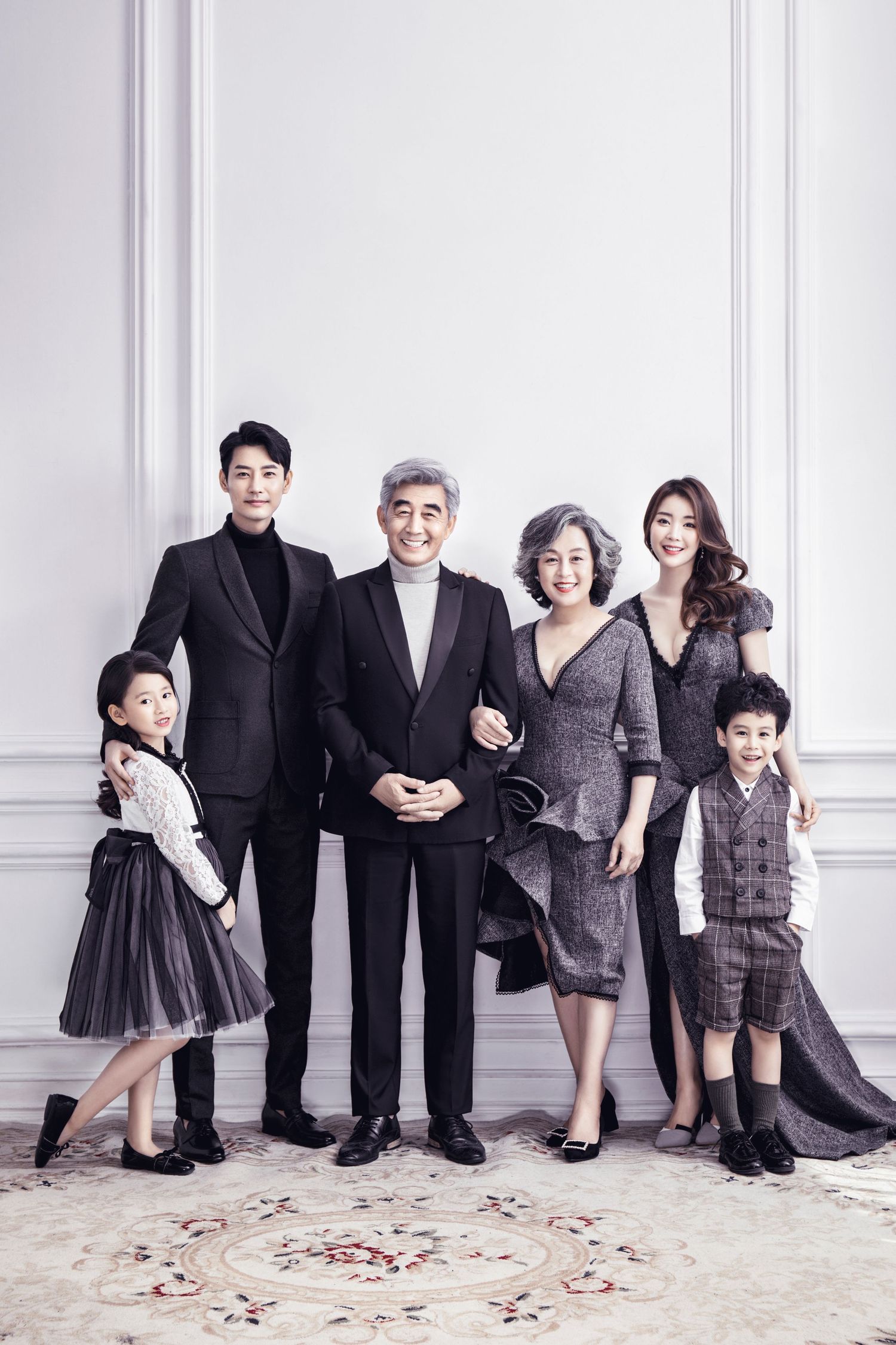 Elegant multigenerational Asian family portrait with grandparents, adult children, and grandkids in formal attire against white wall.