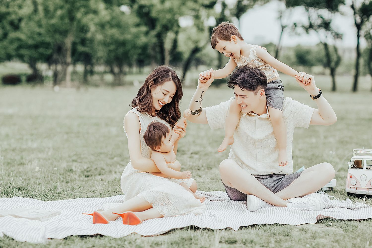 Happy young family enjoying a sunny outdoor picnic on a green lawn with two young children.