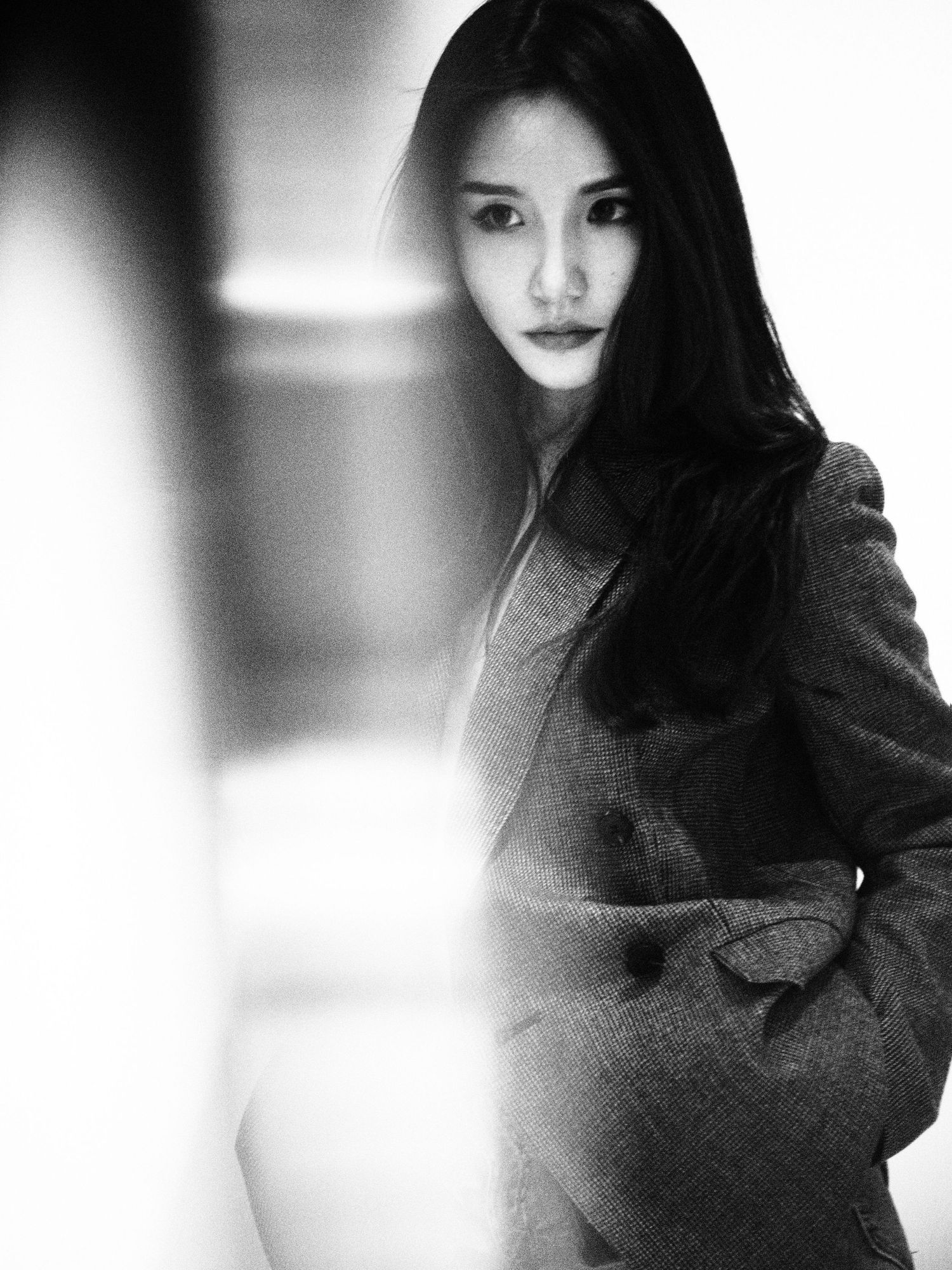 Elegant black and white portrait of an Asian woman in a gray coat with long dark hair in soft light.