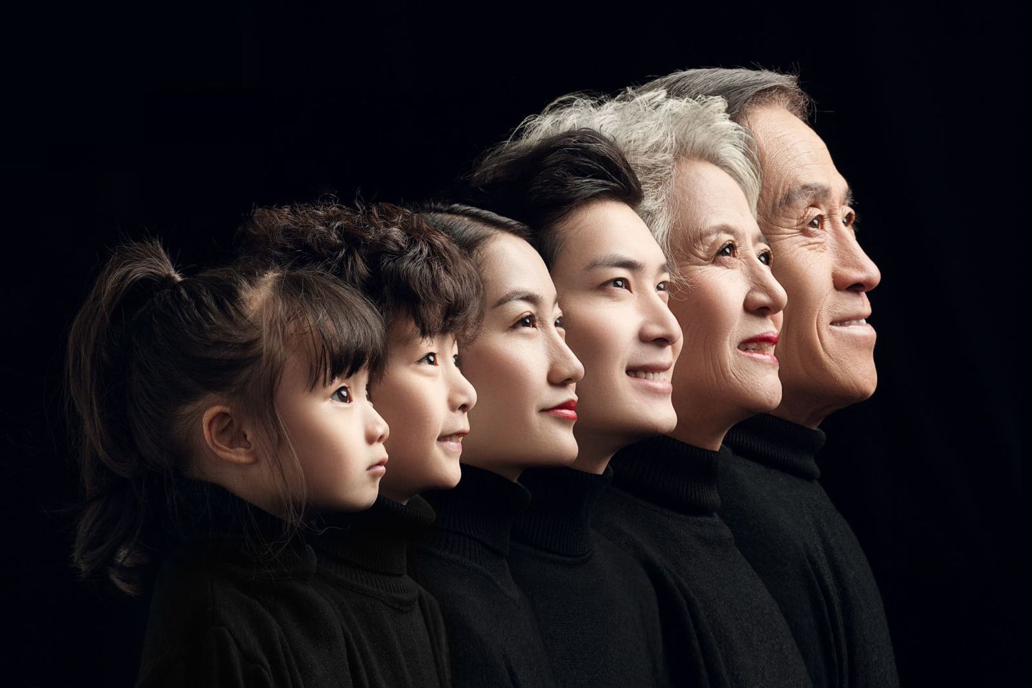 Multi-generational Asian family of five in black turtlenecks posed in profile view against dark background.