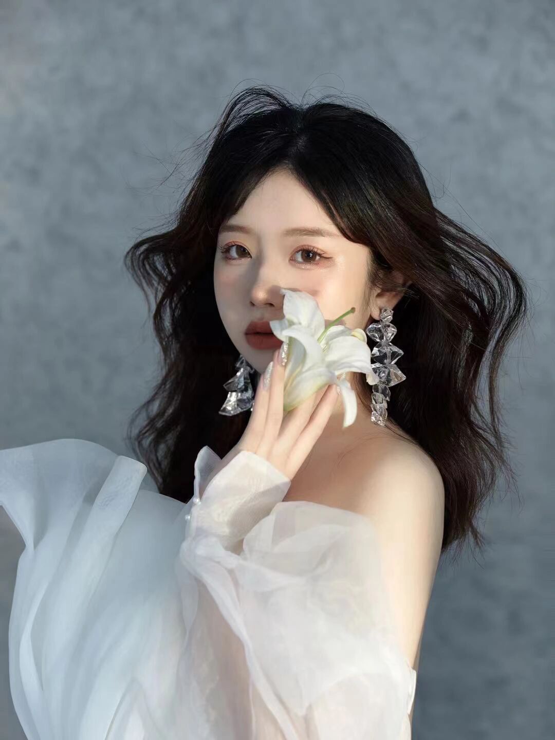 Young woman in white tulle dress holding white lily flower close to face with crystal earrings.
