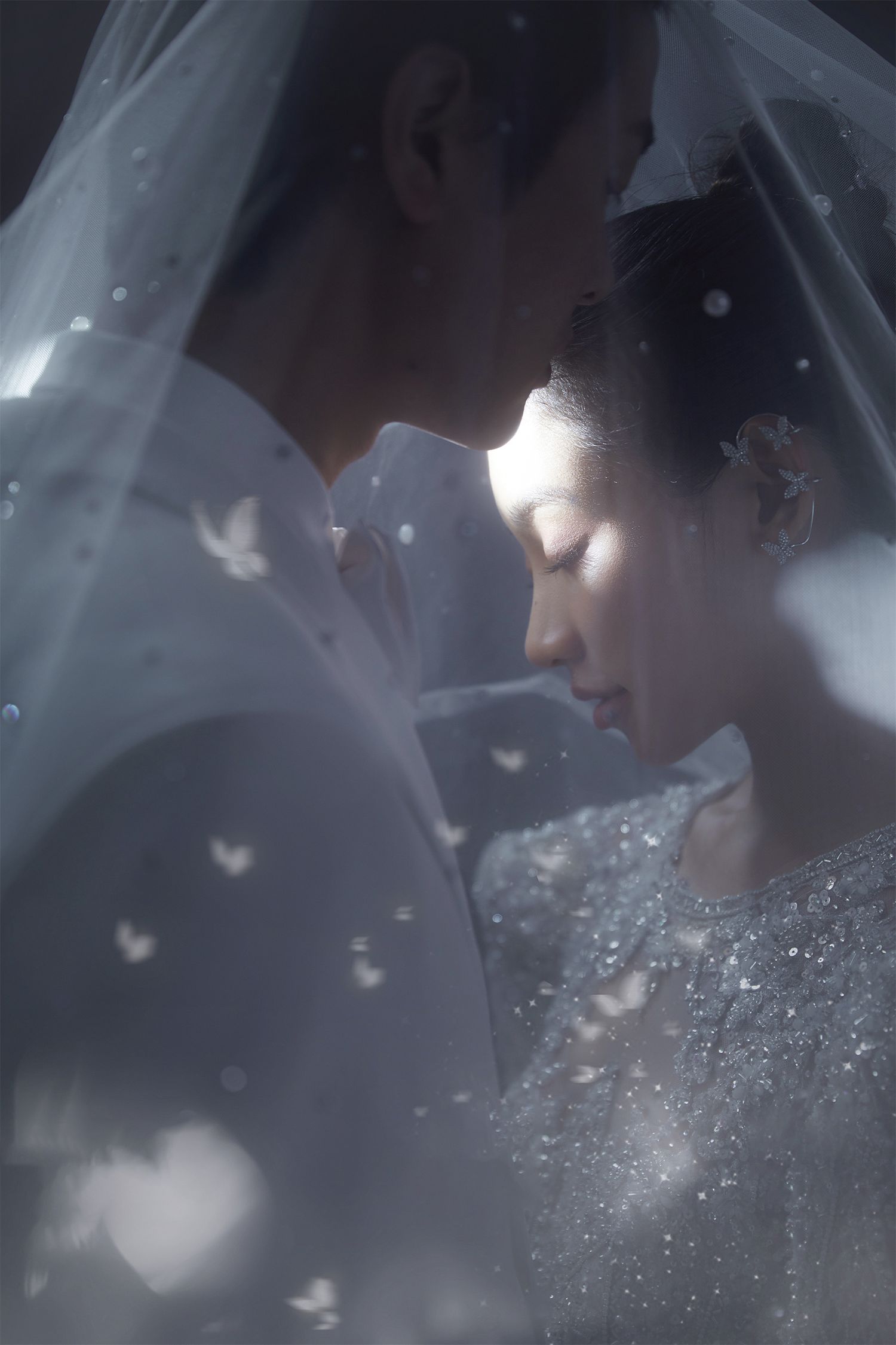 Romantic couple sharing intimate moment under wedding veil with sparkling heart-shaped bokeh lights.