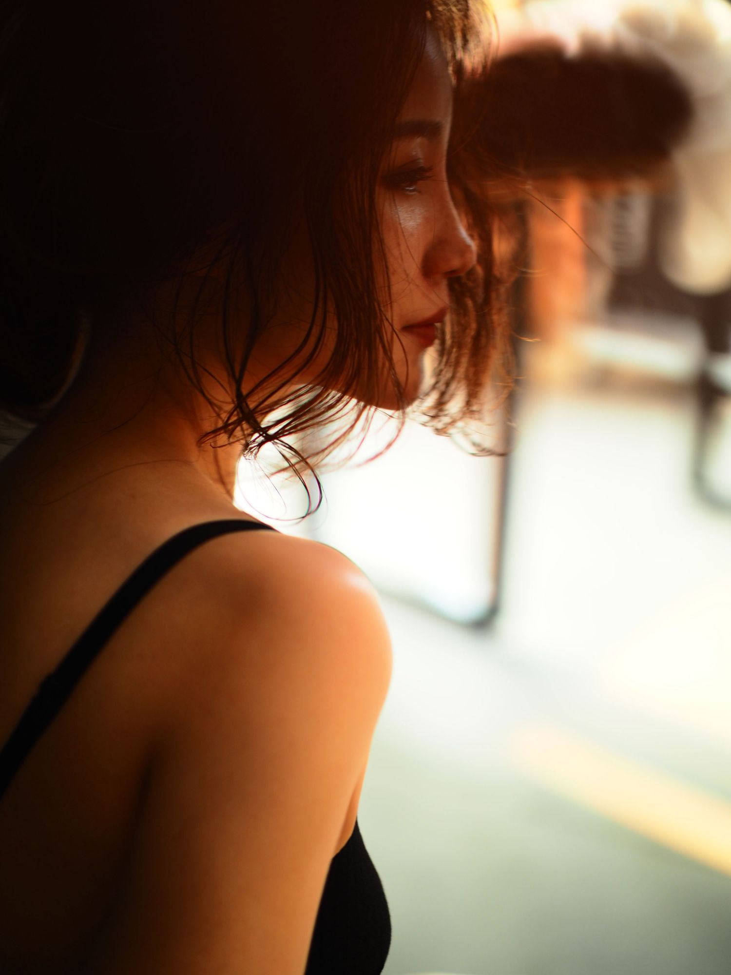 Side profile of an Asian woman with short hair wearing a black camisole bathed in warm golden hour light.