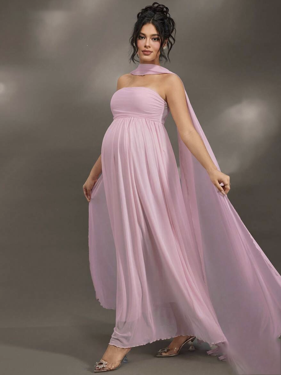 Pregnant woman in flowing pink halter maxi dress with cape detail and embellished heels.