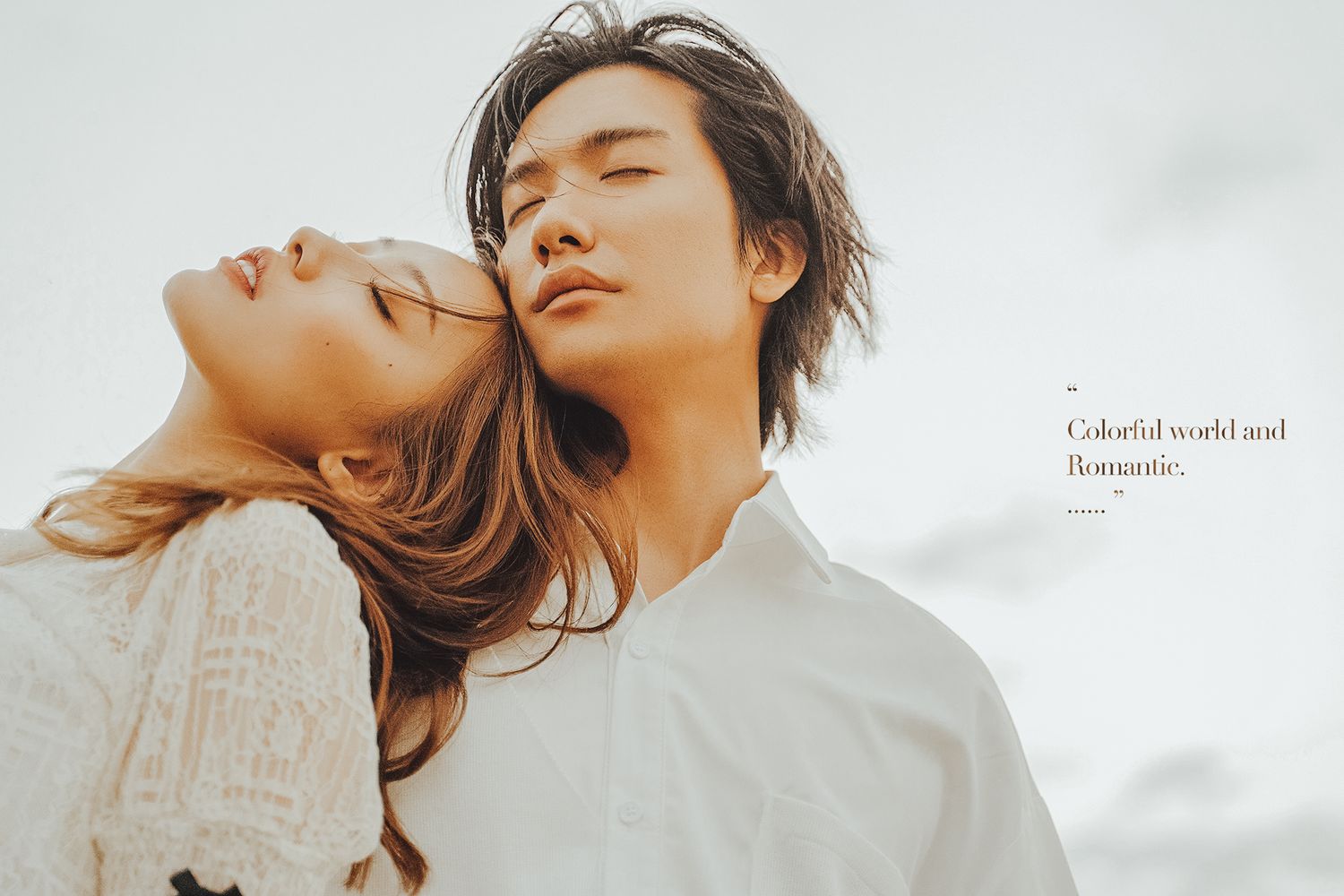 Romantic couple in white clothing with eyes closed outdoors.