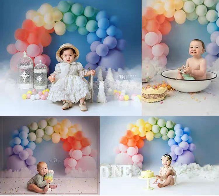 Four babies celebrate first birthdays with colorful rainbow balloon arch backdrop in professional photo studio settings.