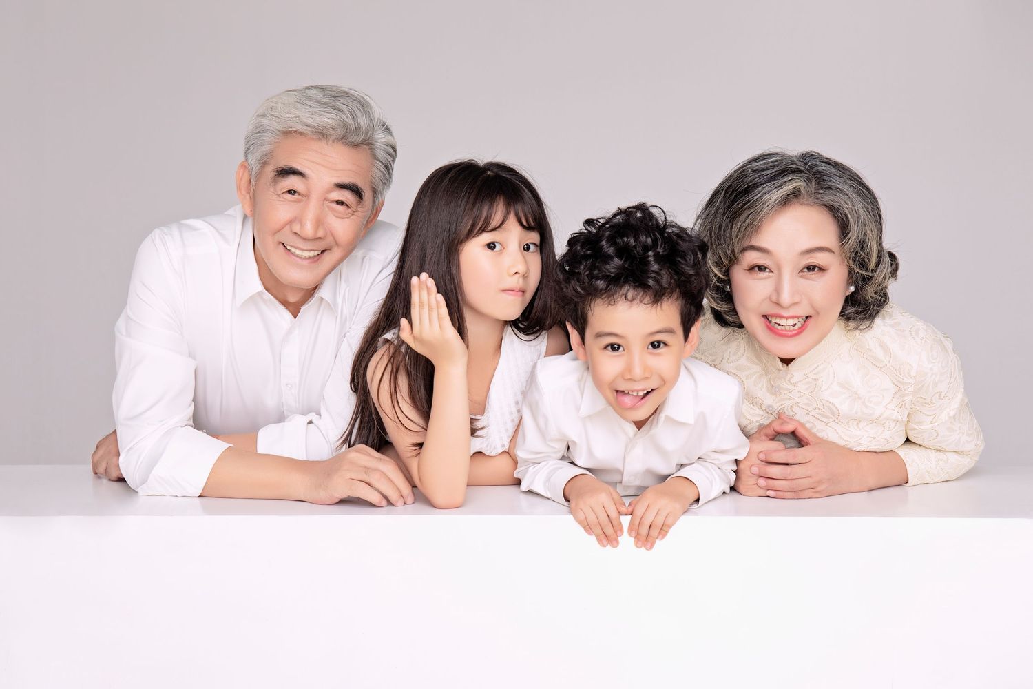 Two Asian grandparents in white outfits smiling with two young grandchildren in a studio portrait.
