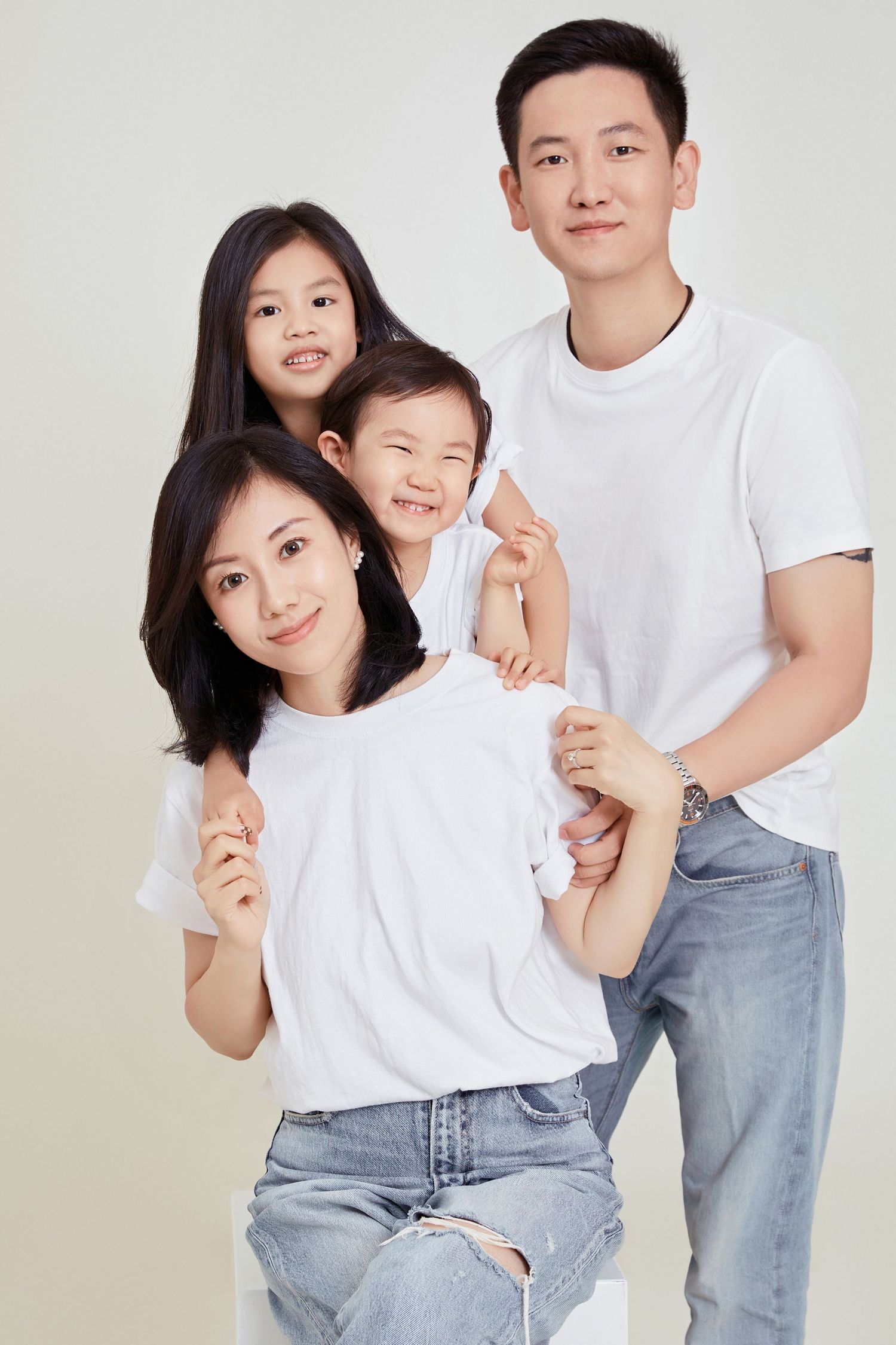 Happy Asian family of four in matching white t-shirts and jeans posing together in a bright studio portrait.