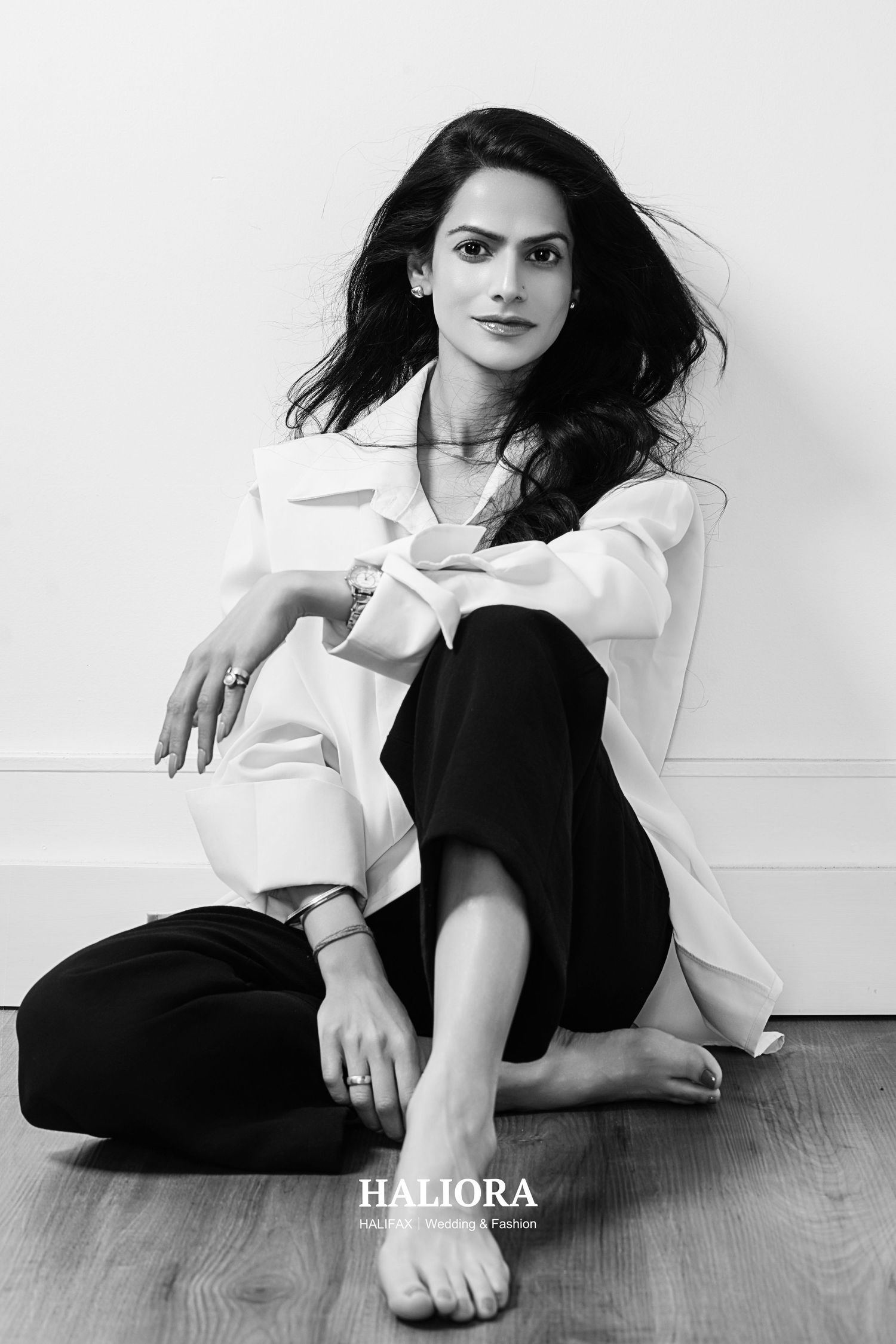 Black and white fashion portrait of woman in white blazer and black pants sitting on floor, studio shot.