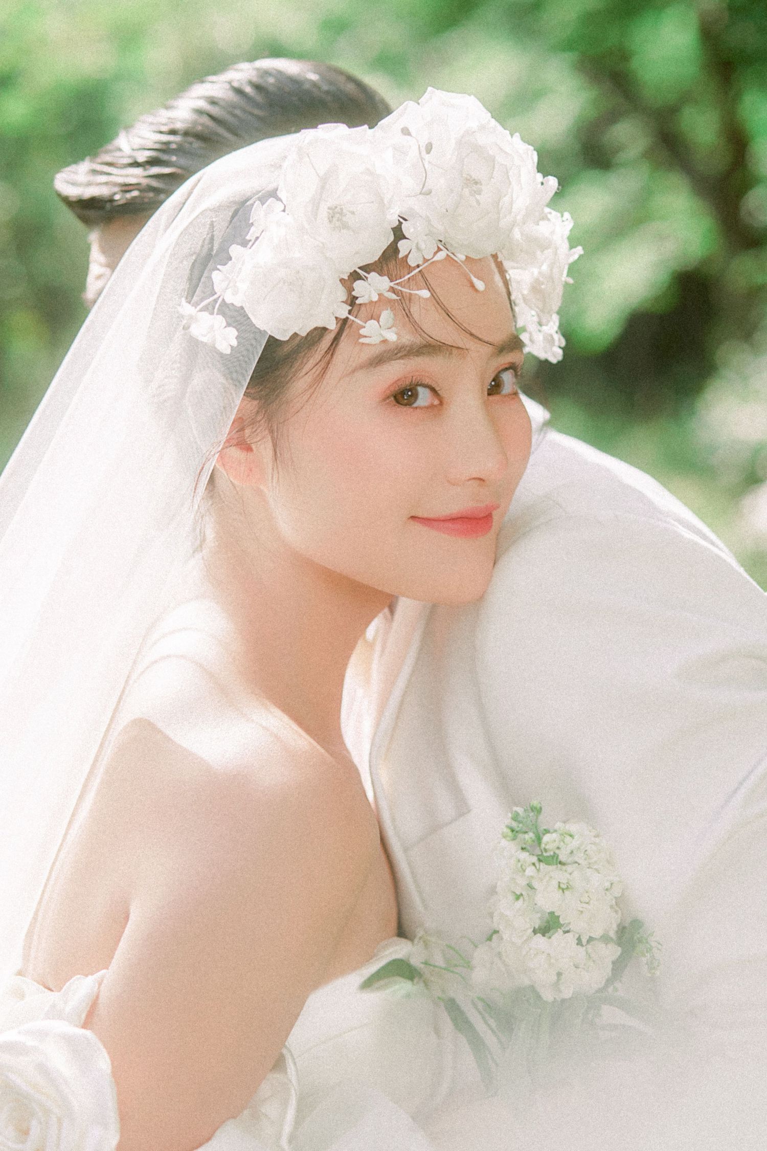Beautiful Asian bride in white floral crown and veil holding white bouquet, romantic outdoor wedding portrait.