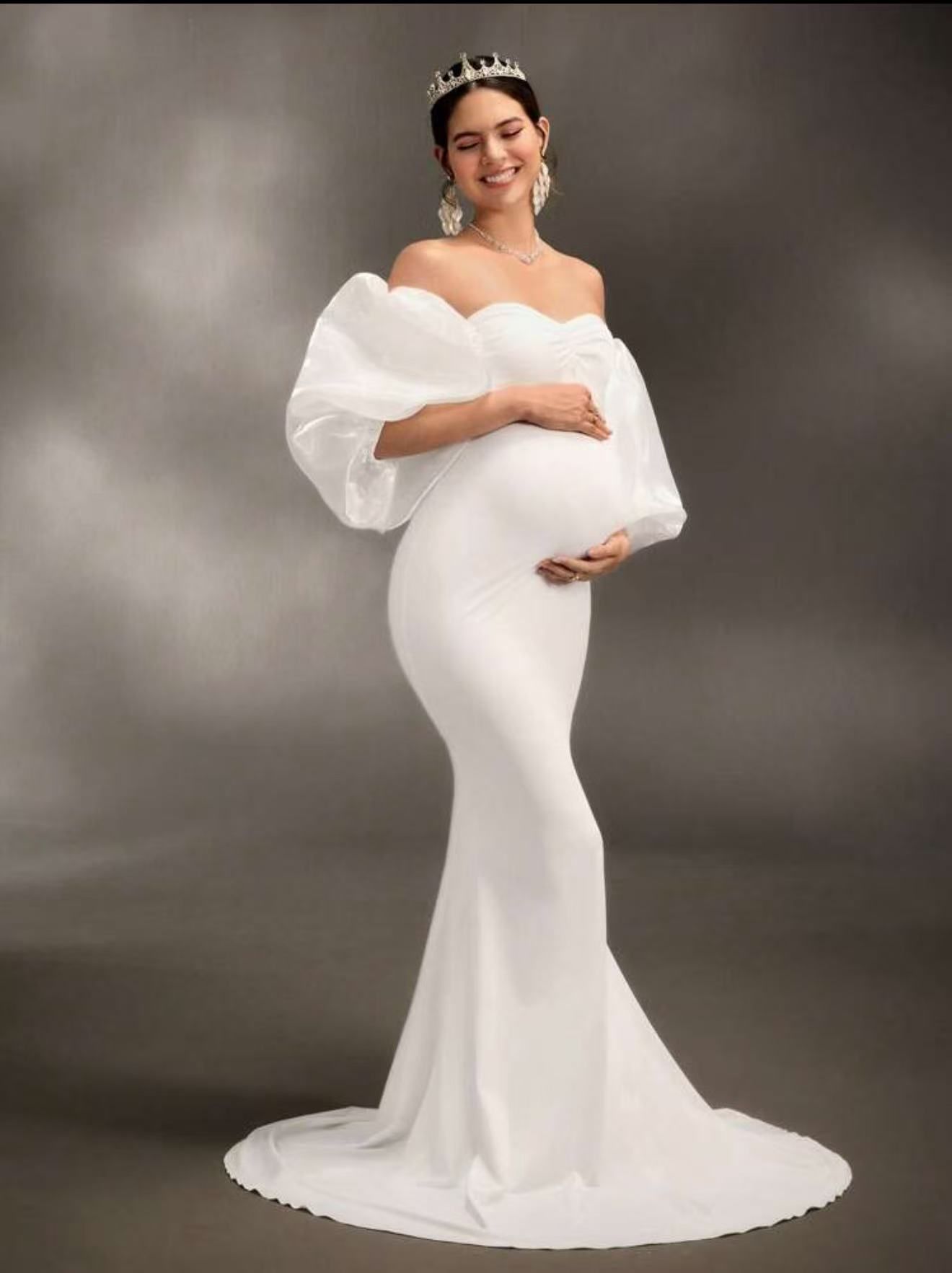 Pregnant woman in white off-shoulder mermaid maternity gown with puff sleeves.