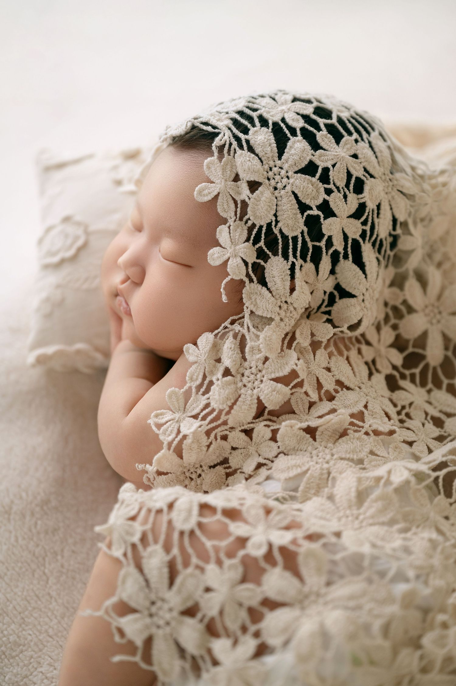 Close-up of sleeping newborn draped in delicate cream floral lace wrap.