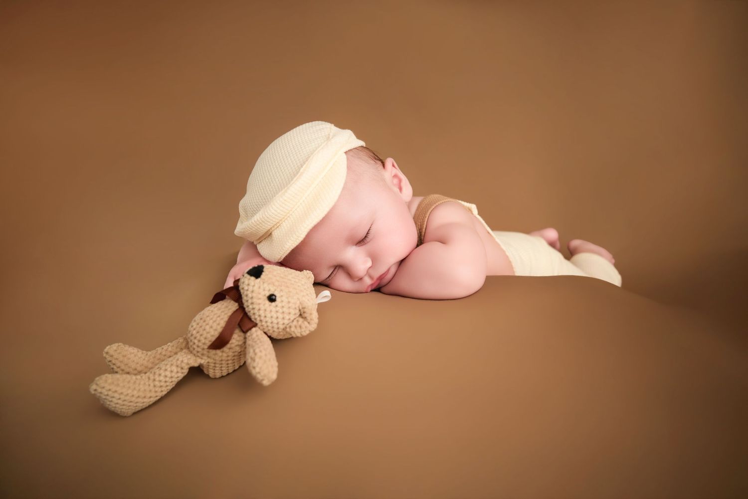 Sleeping newborn baby with white headband cuddling a knit bunny toy on a warm brown background.